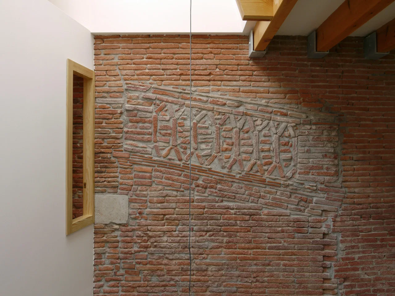 An exposed red brick wall features a decorative geometric masonry inlay, flanked by a light wood-framed mirror and overhead wooden beams.