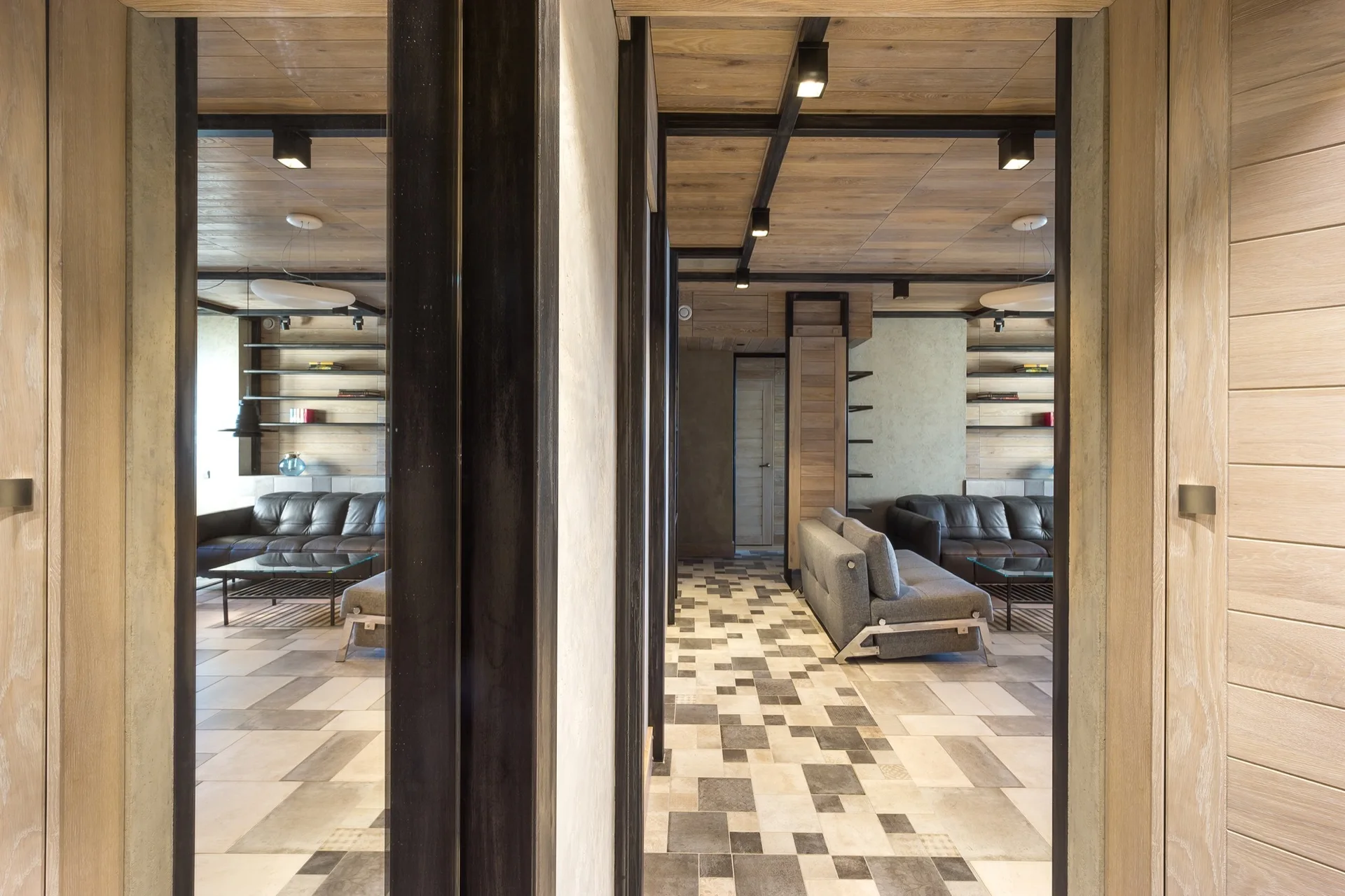 A modern living room featuring a warm wood plank ceiling with dark metal framing, gray sofas, and geometric block pattern floor tiles.