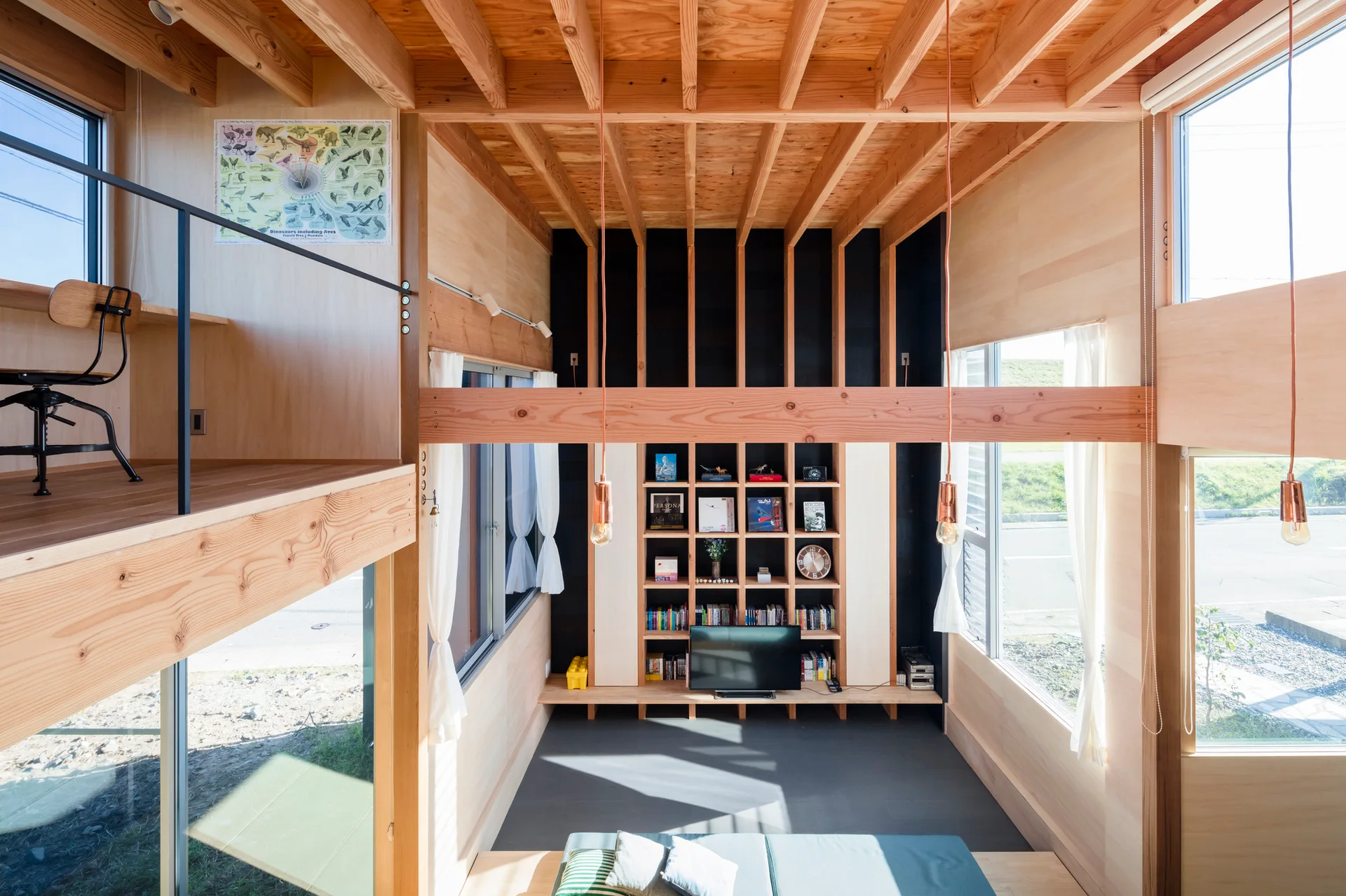 A modern double-height living room featuring an exposed timber joist ceiling, a tall grid bookcase against a black wall, and a mezzanine workspace.