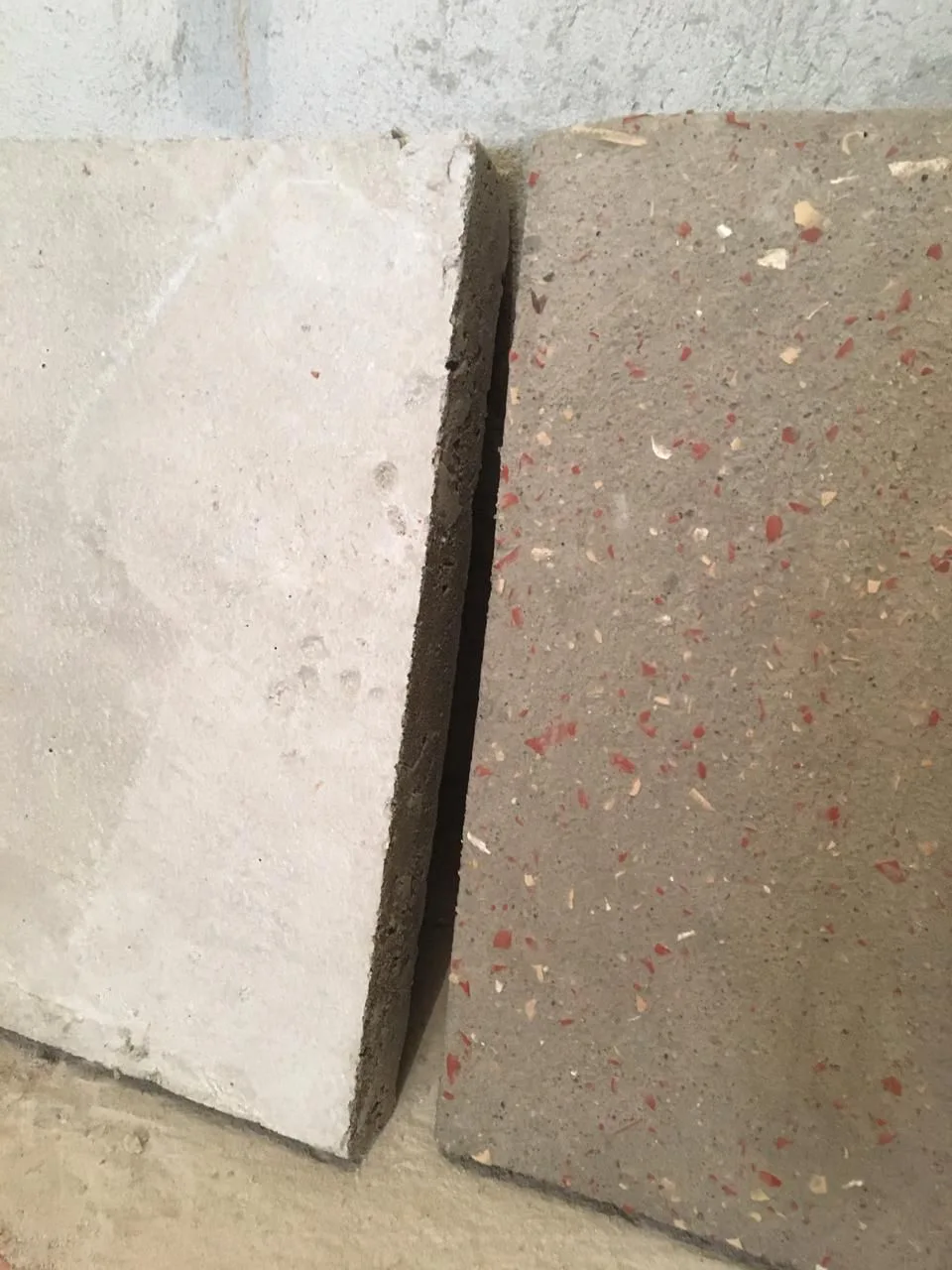 Two rectangular material sample tiles sit side-by-side, showcasing a plain grey concrete slab next to a textured terrazzo tile with red and beige flecks.