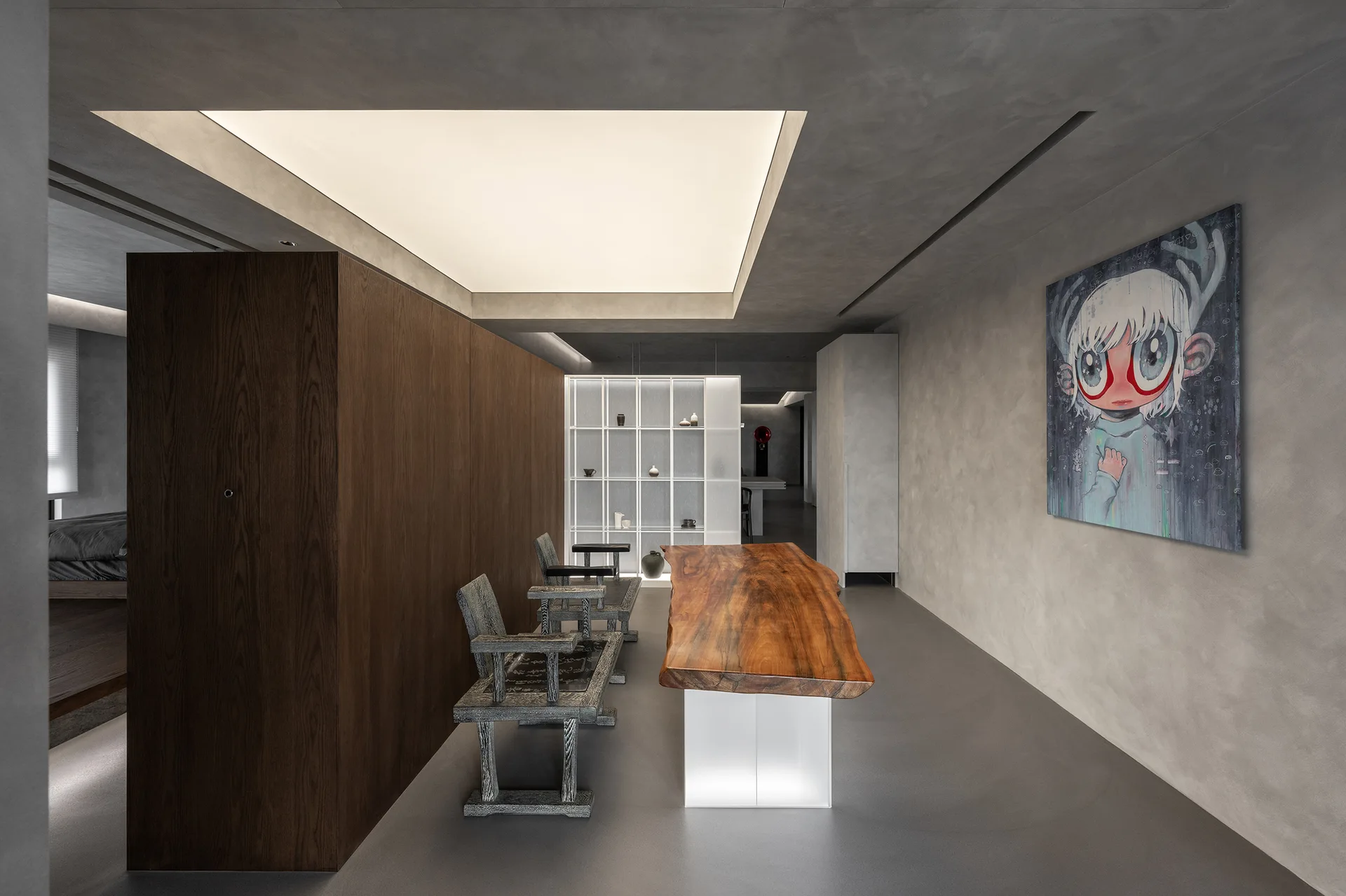 A minimalist room featuring a live-edge wood table, rustic wooden chairs, a dark partition wall, and a large glowing ceiling light panel.