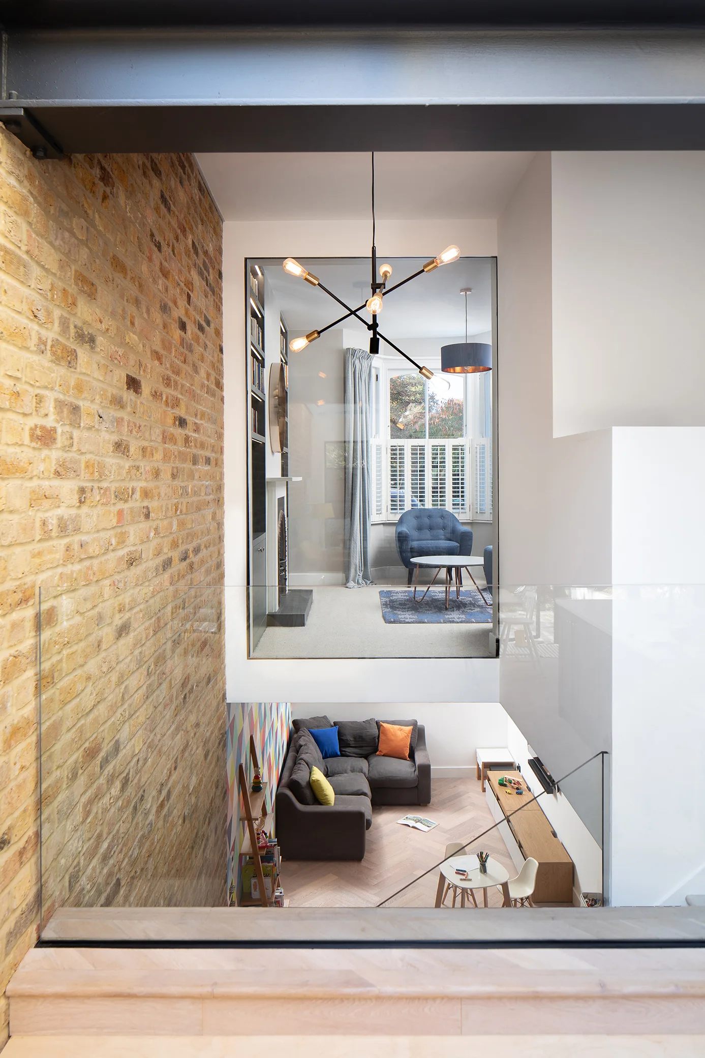 A split-level home interior with an exposed brick wall, a glass staircase railing, and two distinct living areas.