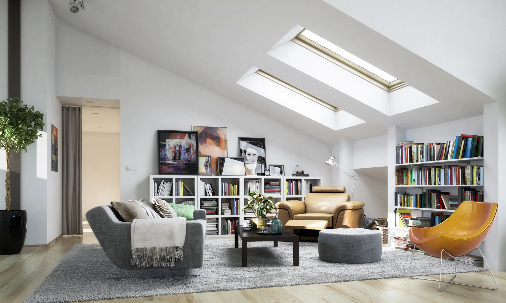 A bright attic living room with skylights, built-in bookshelves, a grey sofa, a tan armchair, and artwork leaning on the low shelves.