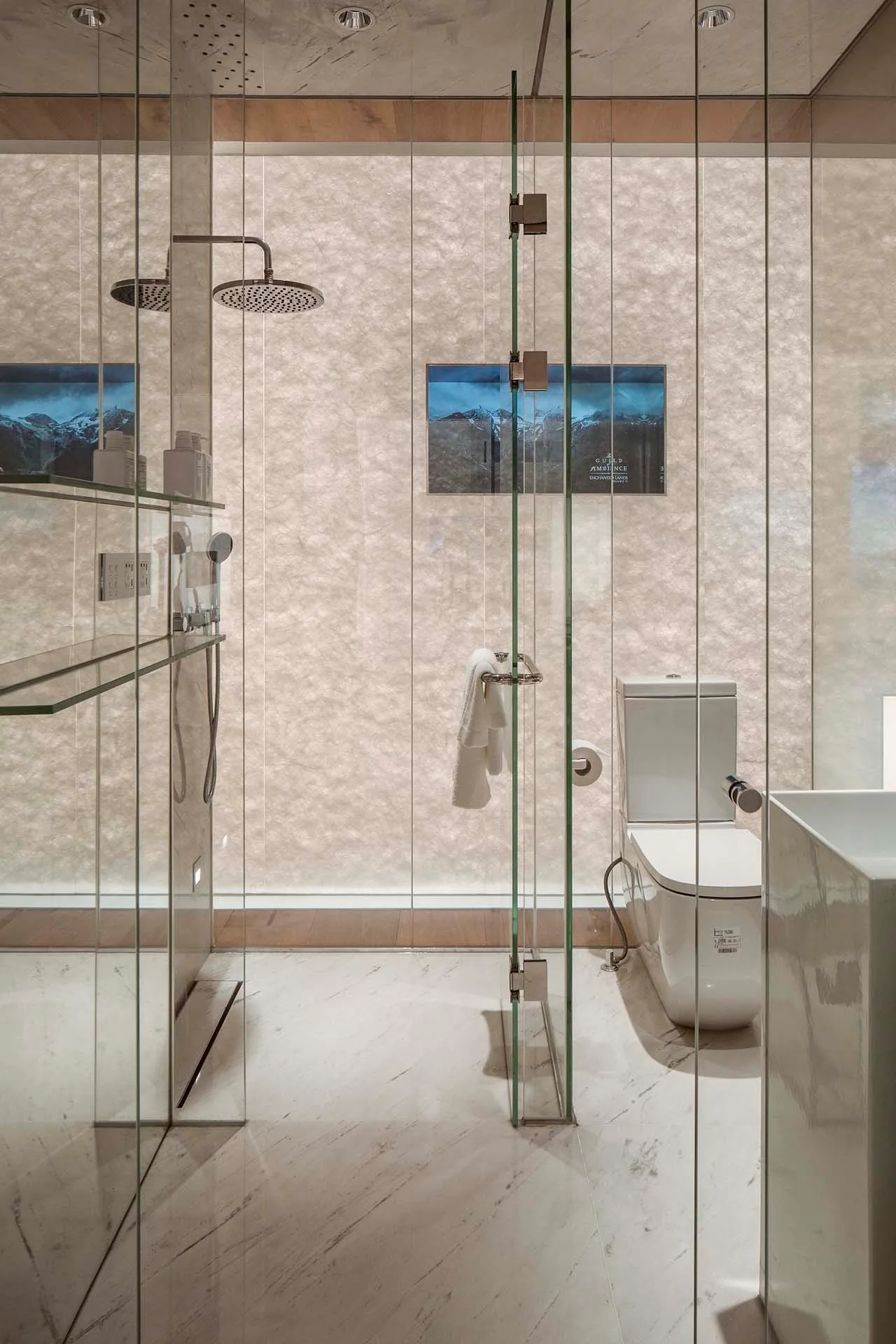 A modern bathroom features a frameless glass shower enclosure with a backlit textured stone wall, a white toilet, and polished marble flooring.