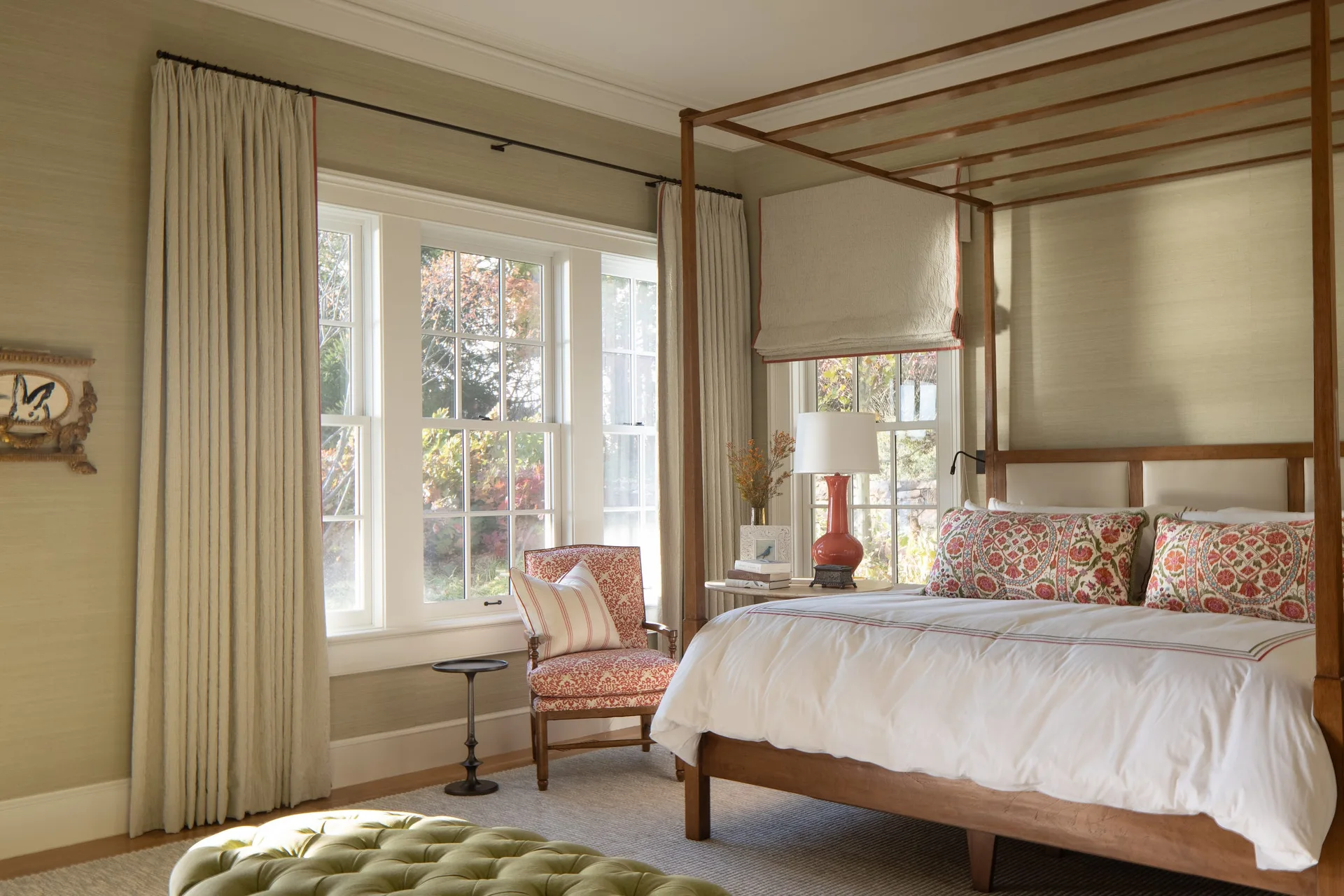A traditional bedroom featuring a wooden four-poster bed, a red patterned armchair, and sage green textured wallpaper.