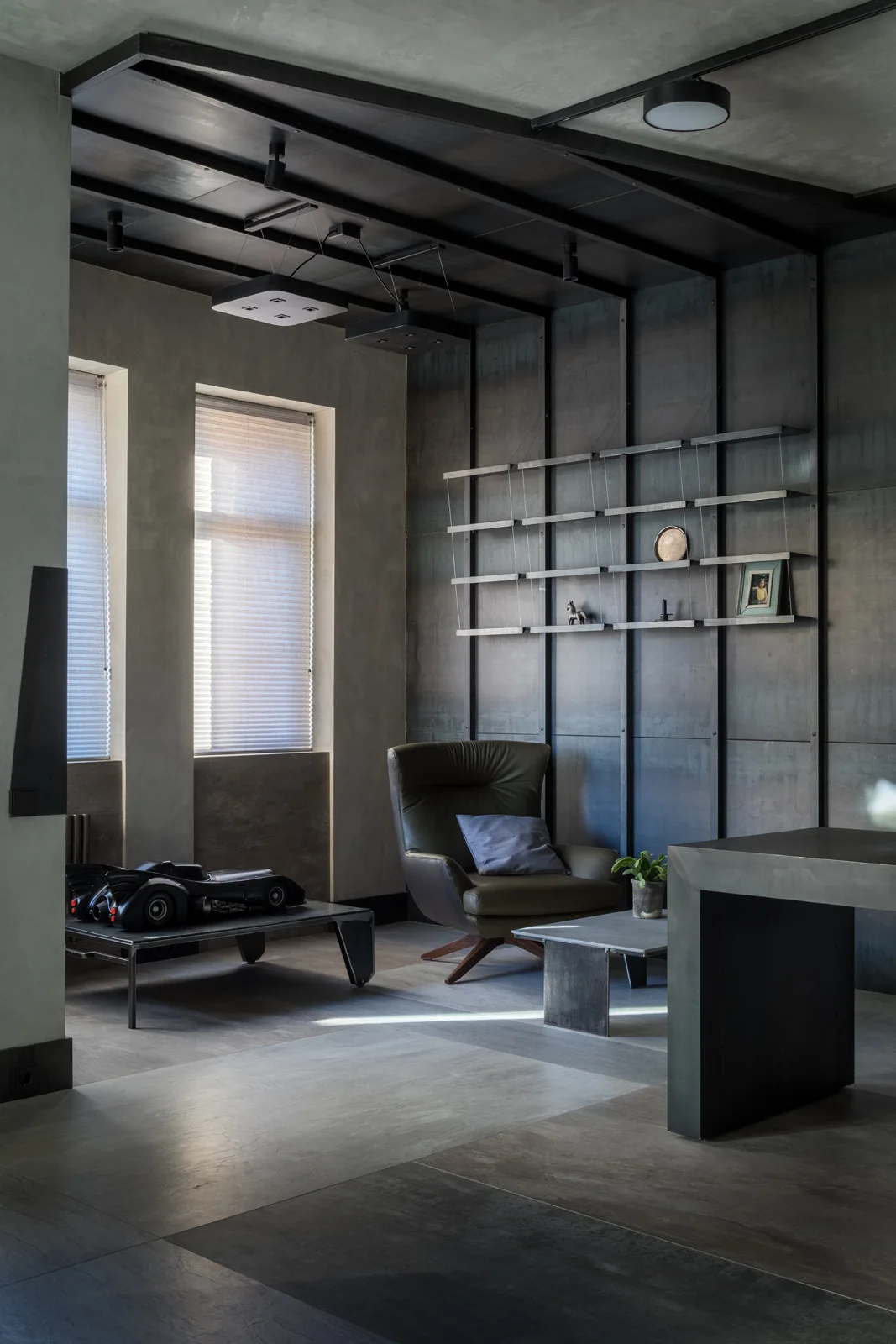 An industrial living space features dark metal wall panels, a minimalist metal shelf unit, and an olive green leather armchair.