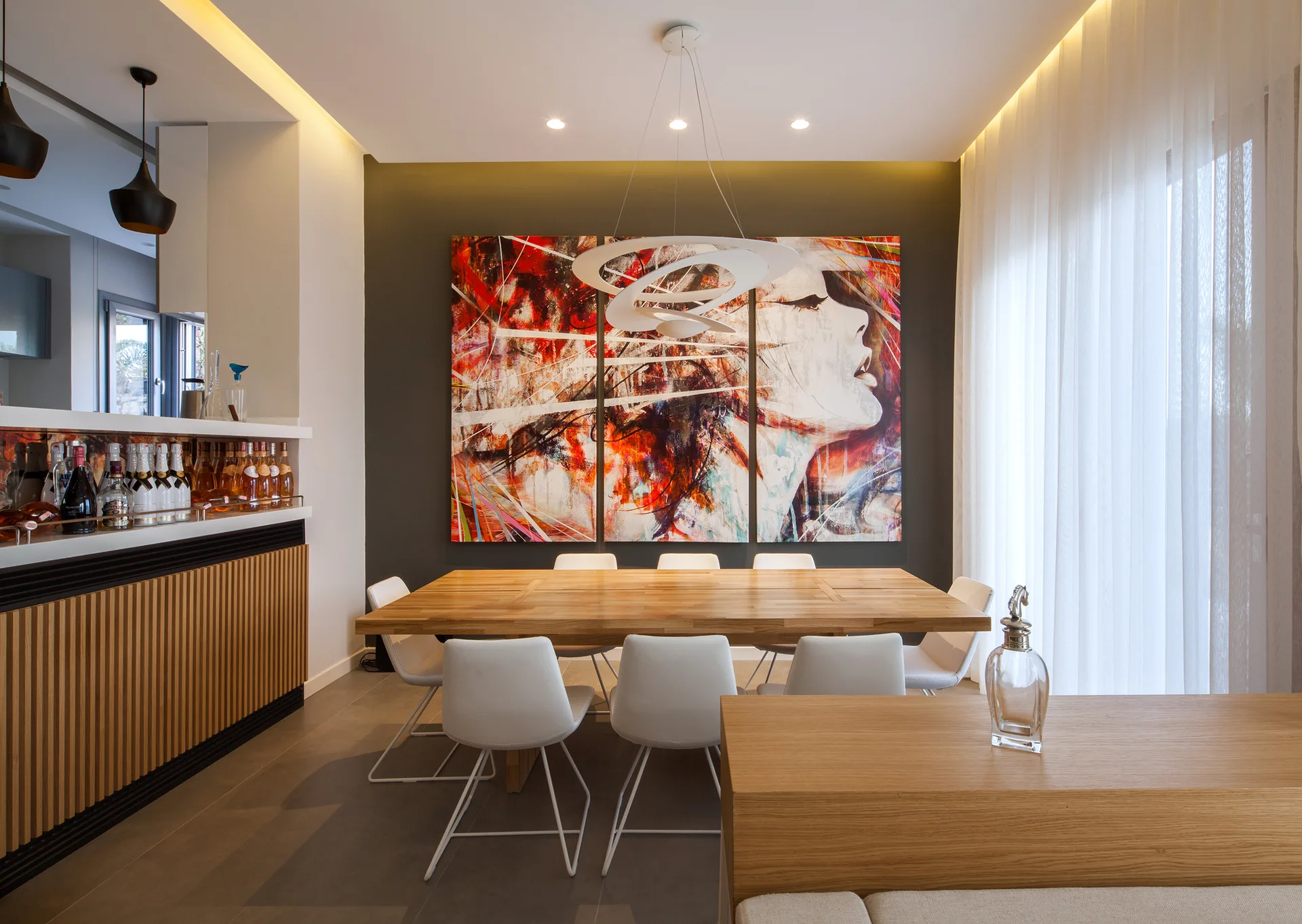 A modern dining room features a light oak table with white chairs set before a large colorful portrait painting on a dark charcoal accent wall.