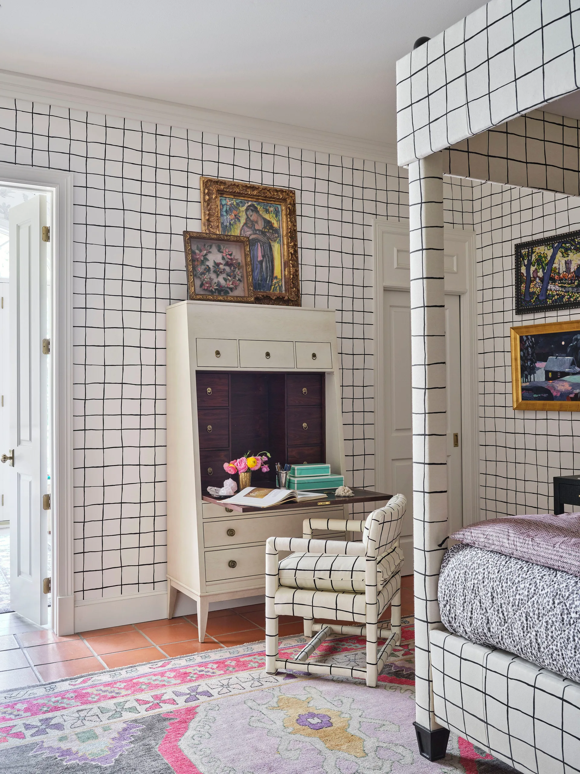 Bedroom featuring black and white grid pattern wallpaper, a matching canopy bed and chair, a cream secretary desk, and a colorful rug.