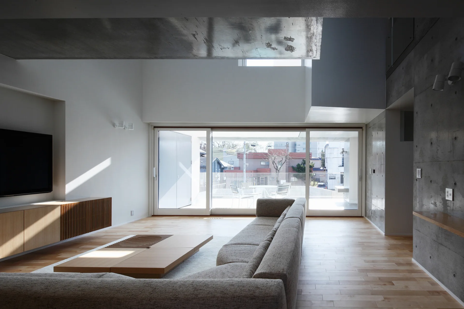 A modern living room features a grey sectional sofa, low wooden coffee table, and large sliding glass doors leading to an outdoor terrace.