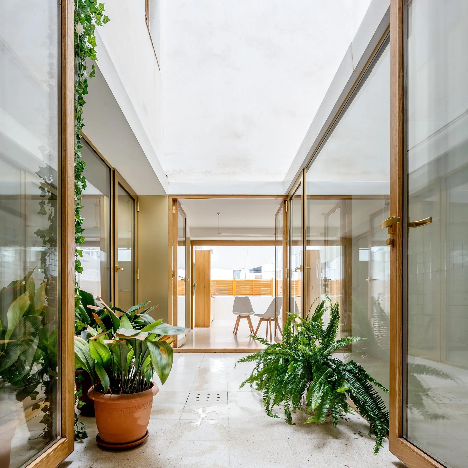 A bright central courtyard with light-colored tile floors features glass doors with wood frames and lush potted plants.