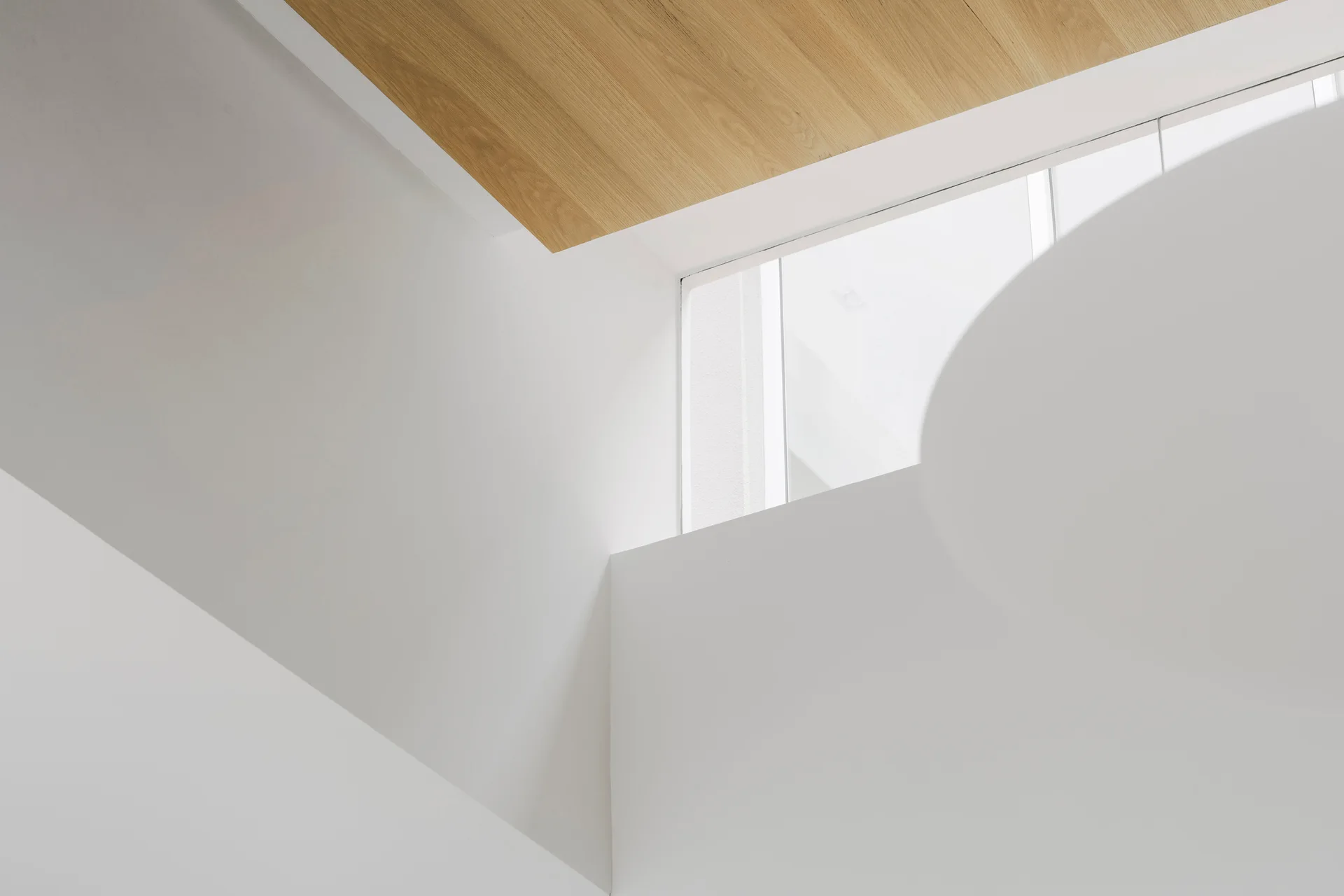 Clean white plaster walls intersect near a light wood-paneled ceiling section and a small high window letting in natural light.