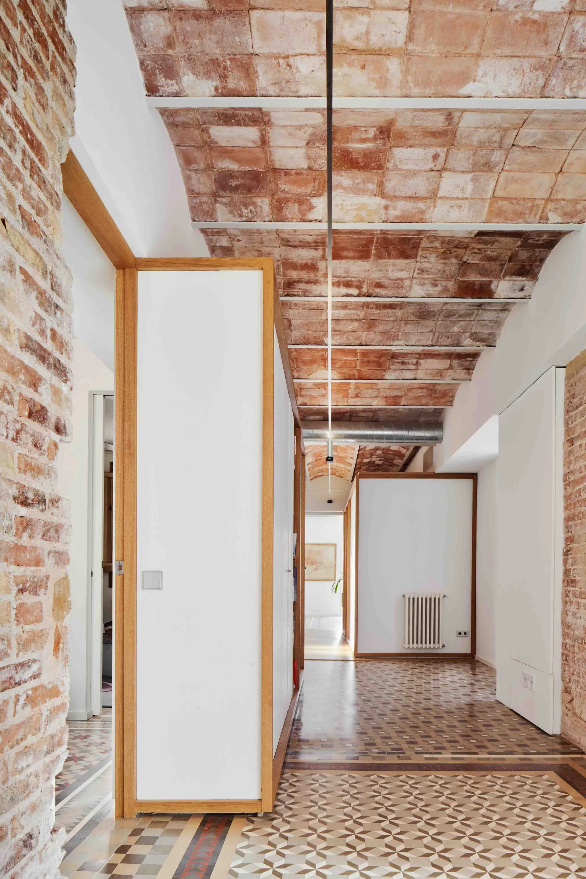 A long hallway features an exposed terracotta vaulted ceiling, patterned tile flooring, and white partition walls with natural wood trim.