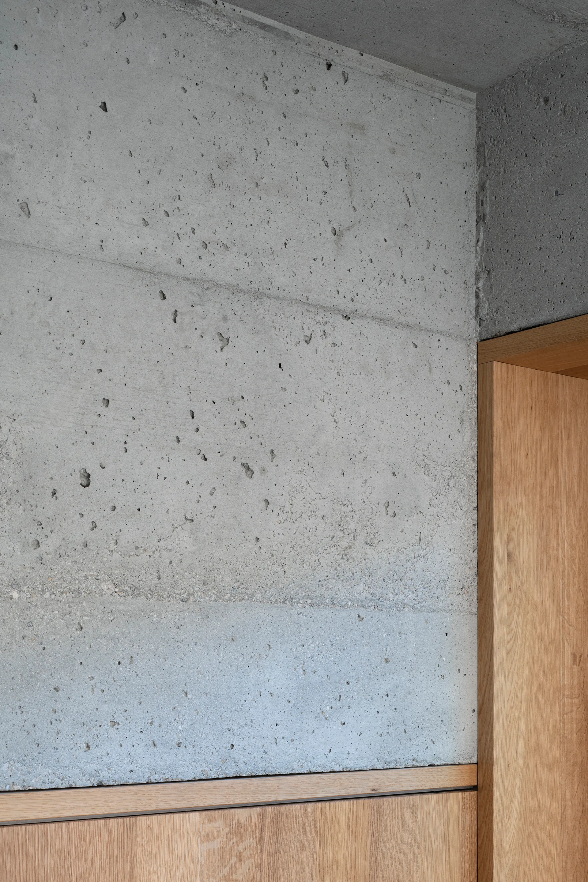 Detail of an industrial interior featuring a textured grey concrete wall adjacent to a smooth natural oak wood door frame and paneling.