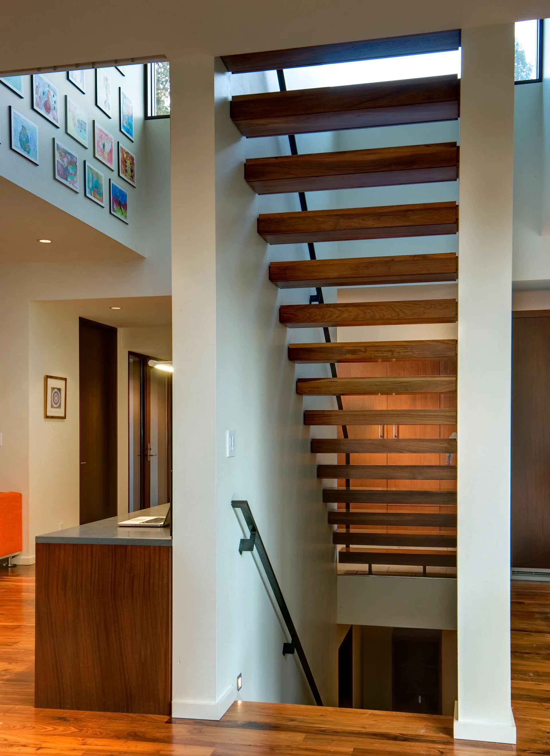 A modern floating wood staircase with thick timber treads and a minimalist black handrail set against white walls.