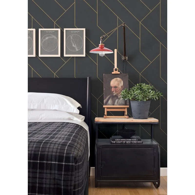 A moody bedroom featuring dark geometric wallpaper, an industrial metal nightstand with a tabletop easel, and a red swing-arm sconce.