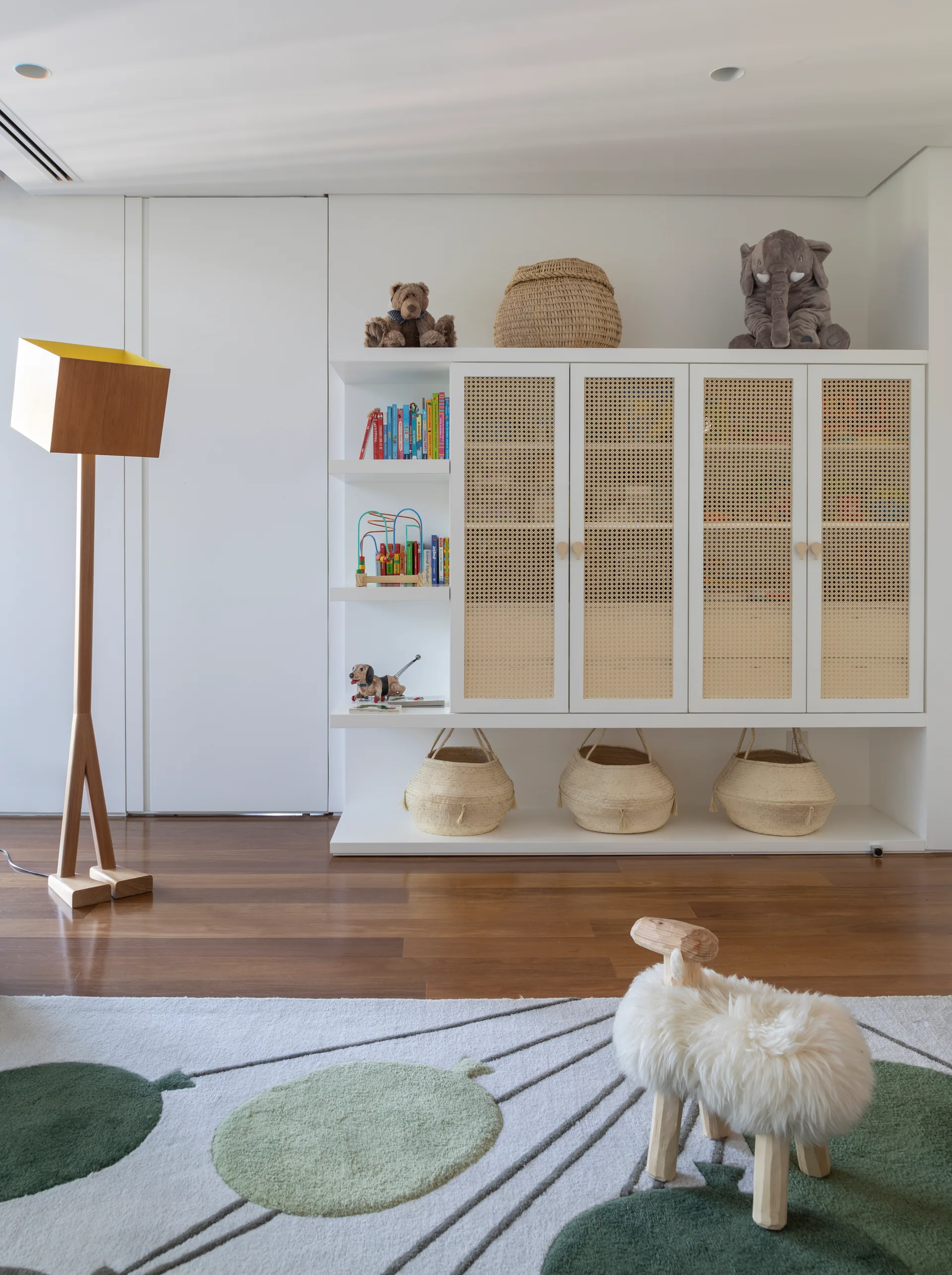 A child's playroom features a white storage cabinet with woven cane doors, three baskets underneath, and a sheep-shaped stool.