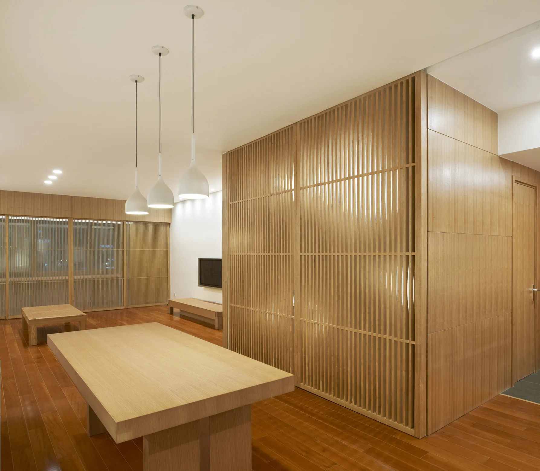 A minimalist dining area featuring a light wood table, three white pendant lights, and a floor-to-ceiling wooden slatted partition screen.