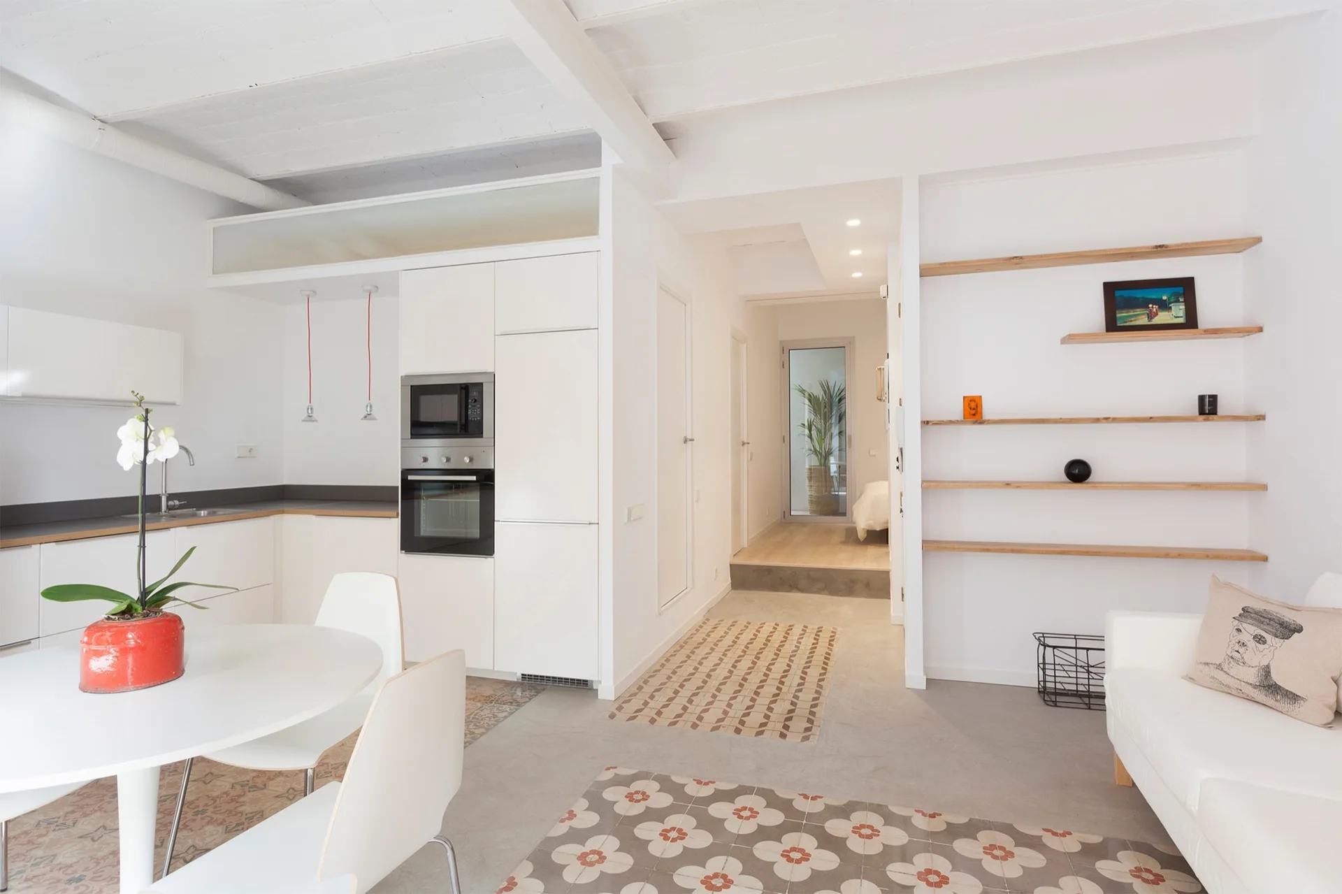 A bright minimalist kitchen features white cabinets, a round dining table, and concrete flooring with patterned decorative tile inserts.