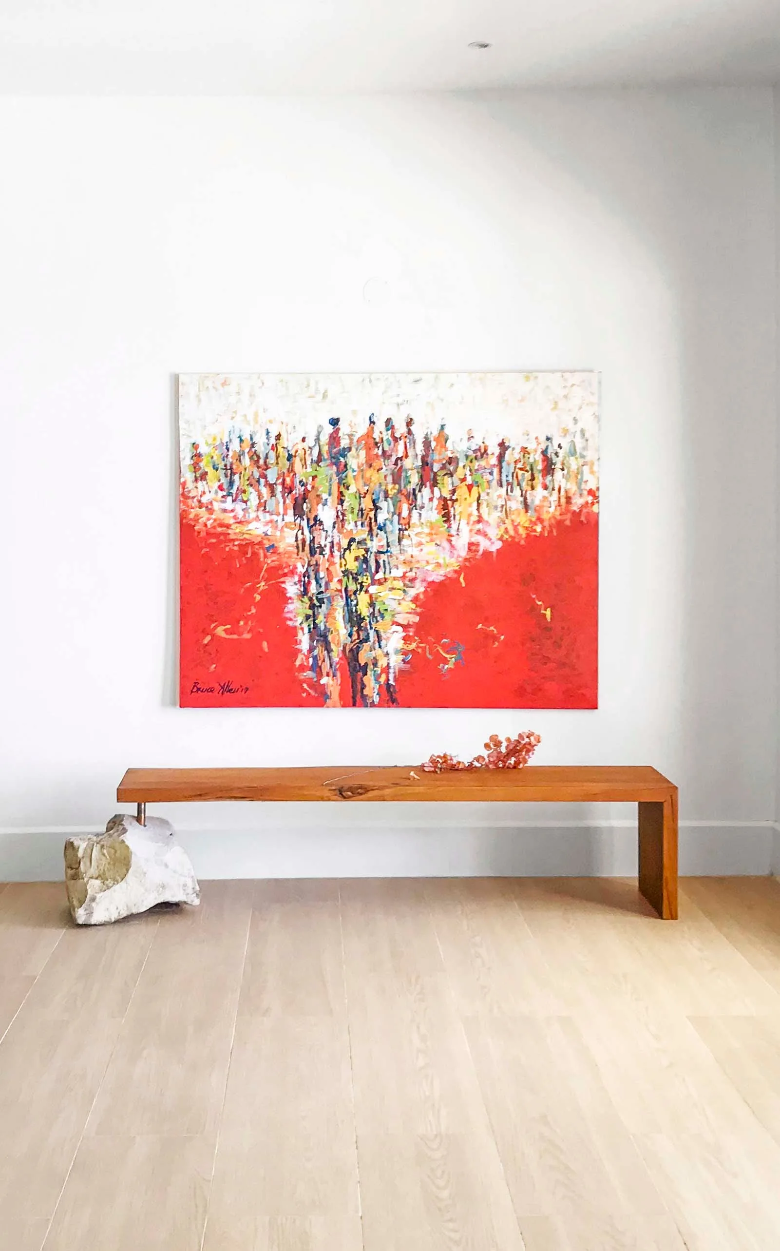 A long wooden bench with a rough stone base sits on light hardwood floors beneath a large red and white abstract painting.
