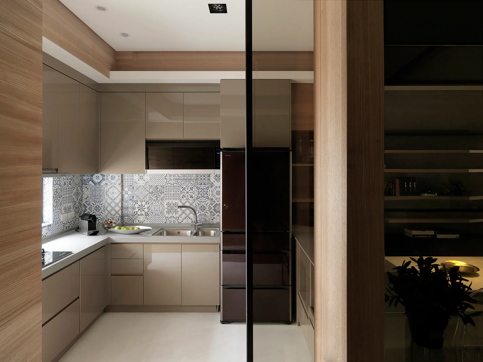 A contemporary kitchen featuring glossy taupe cabinets, a blue and white patterned tile backsplash, and a white countertop.
