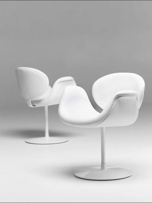 Two white upholstered swivel chairs with organic curved seats and round metal pedestal bases stand against a seamless gray studio background.