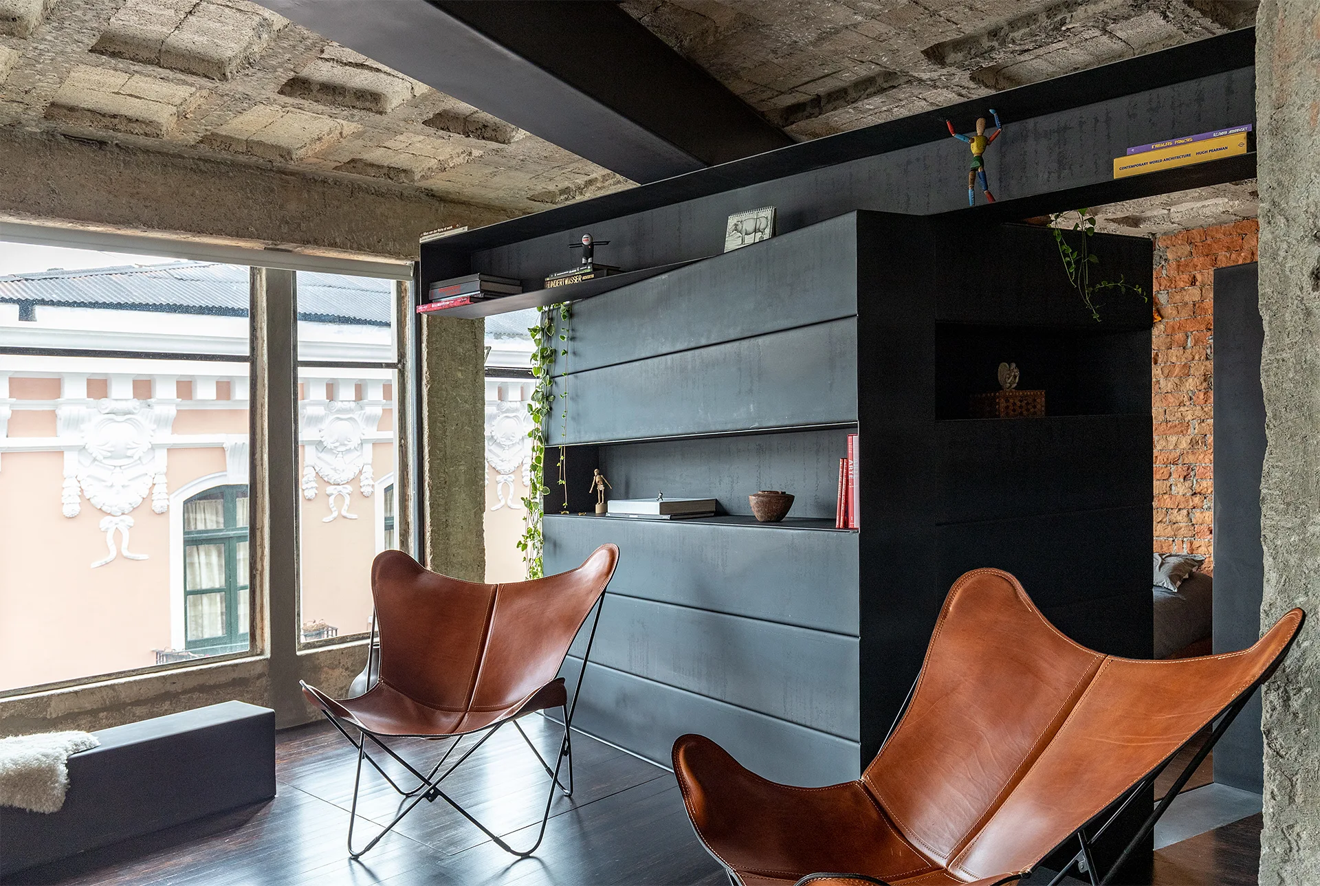 Two tan leather butterfly chairs face a matte dark grey partition wall in an industrial loft with an exposed concrete waffle ceiling.