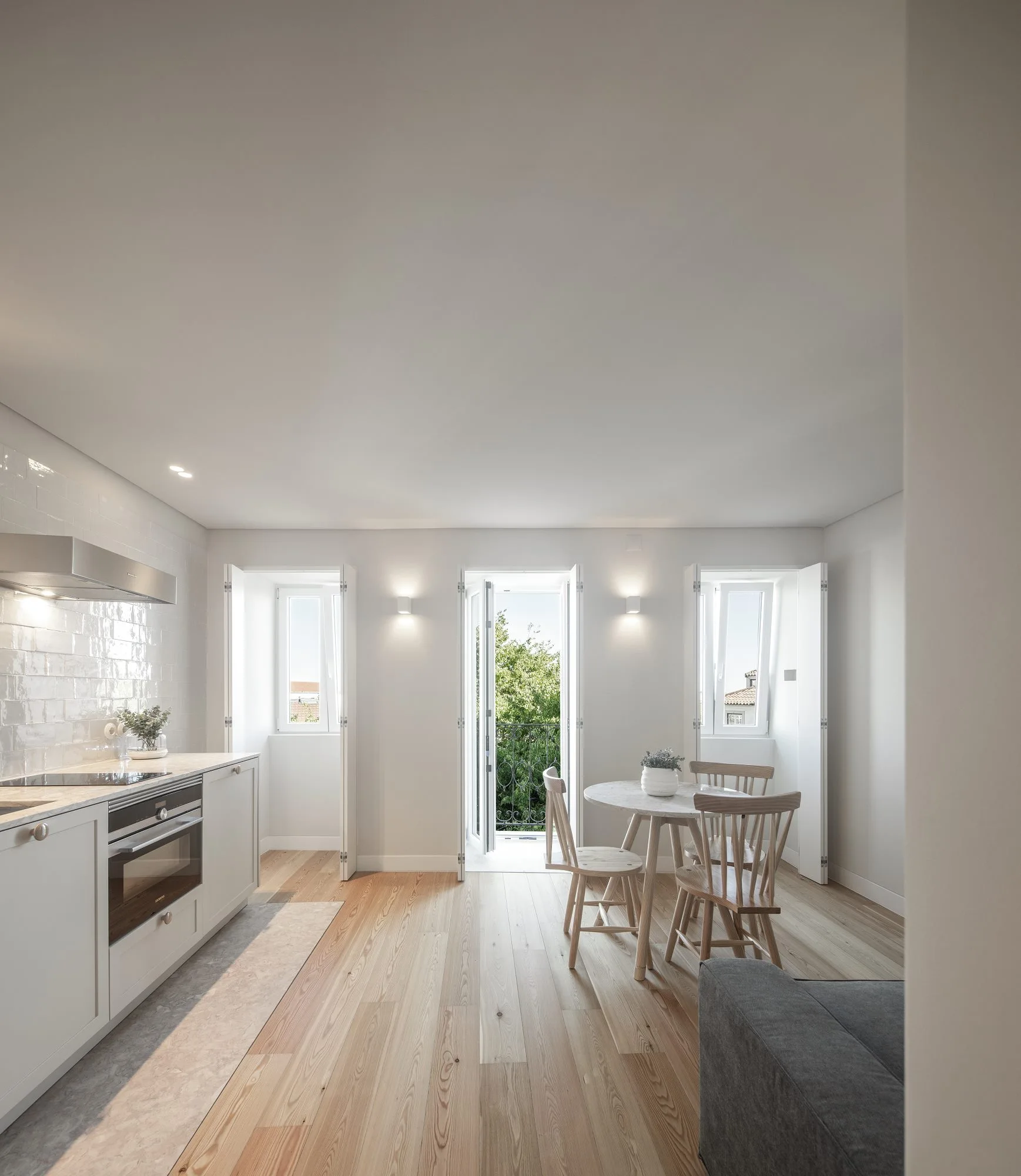 A kitchen and dining area features white cabinets, a round marble table with spindle chairs, and a central balcony door with shutters.
