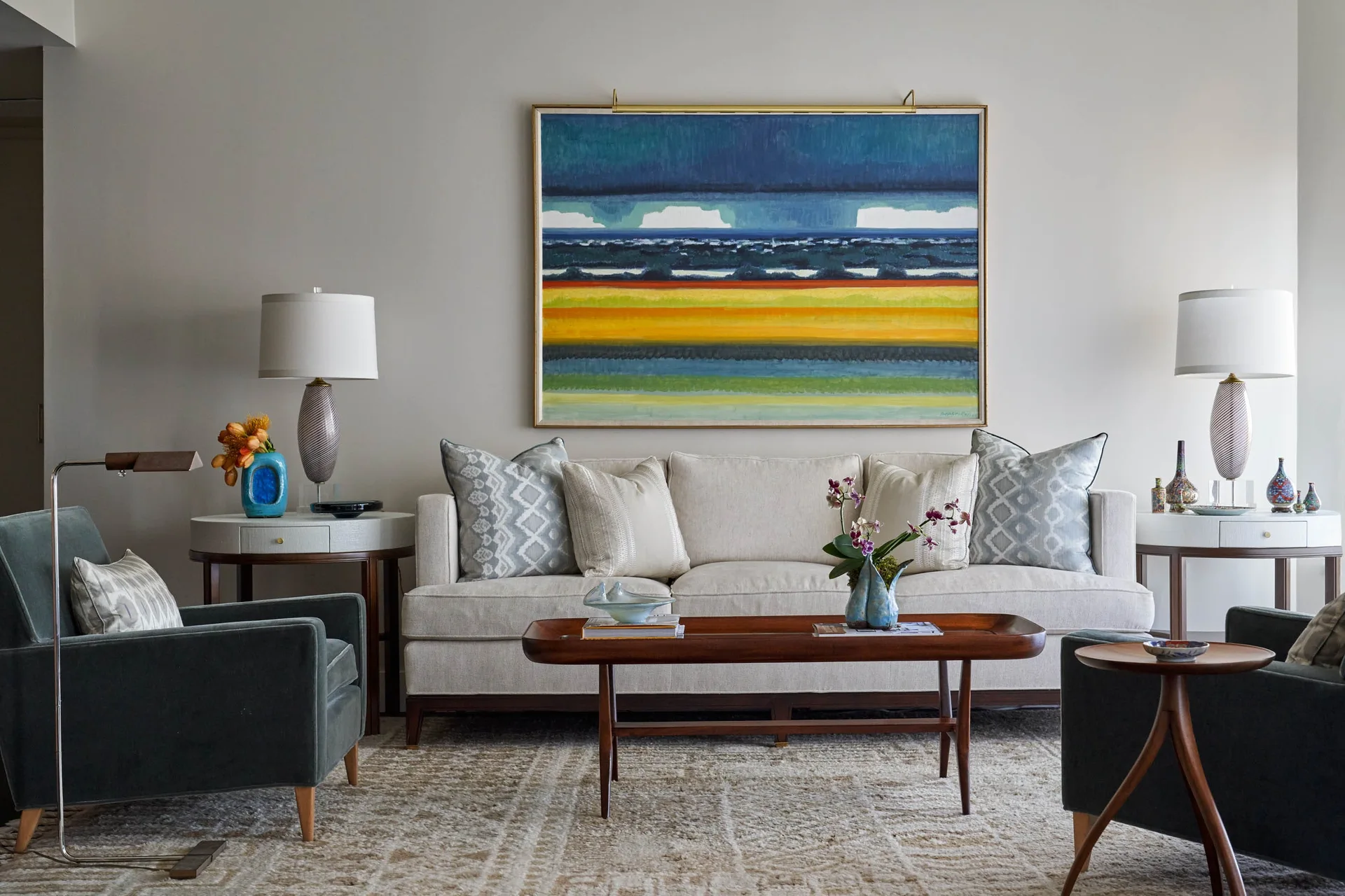 A neutral sofa flanked by identical side tables with lamps is centered under a large abstract painting in a living room.