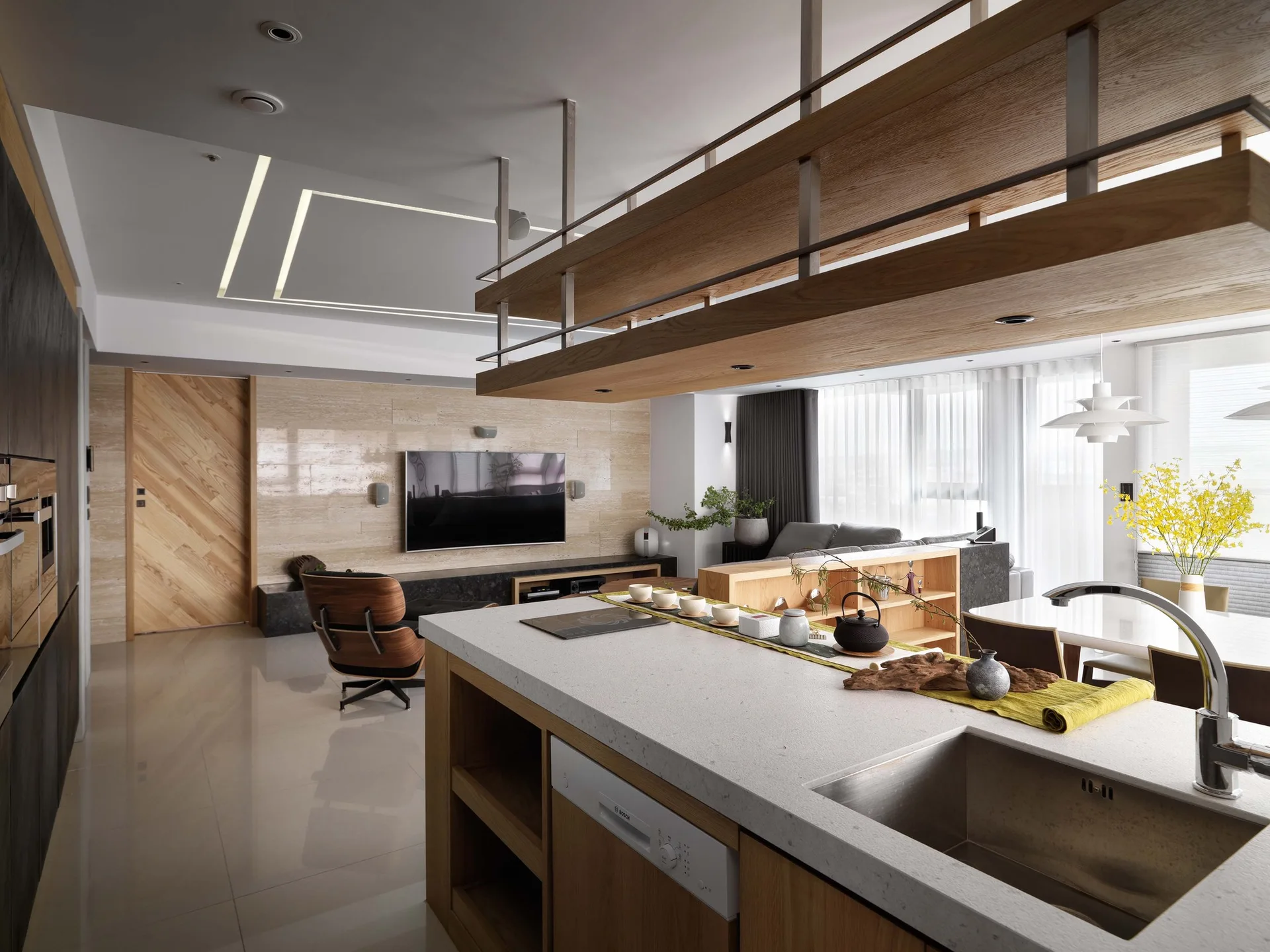 A modern open-plan kitchen and living space featuring a central kitchen island, a suspended wooden ceiling shelf, and a herringbone-patterned sliding door.