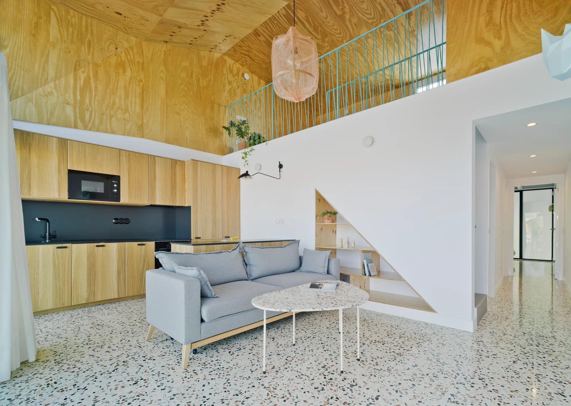 Modern open loft living room featuring a grey sofa, a triangular wall niche with shelves, and a sloped plywood ceiling.