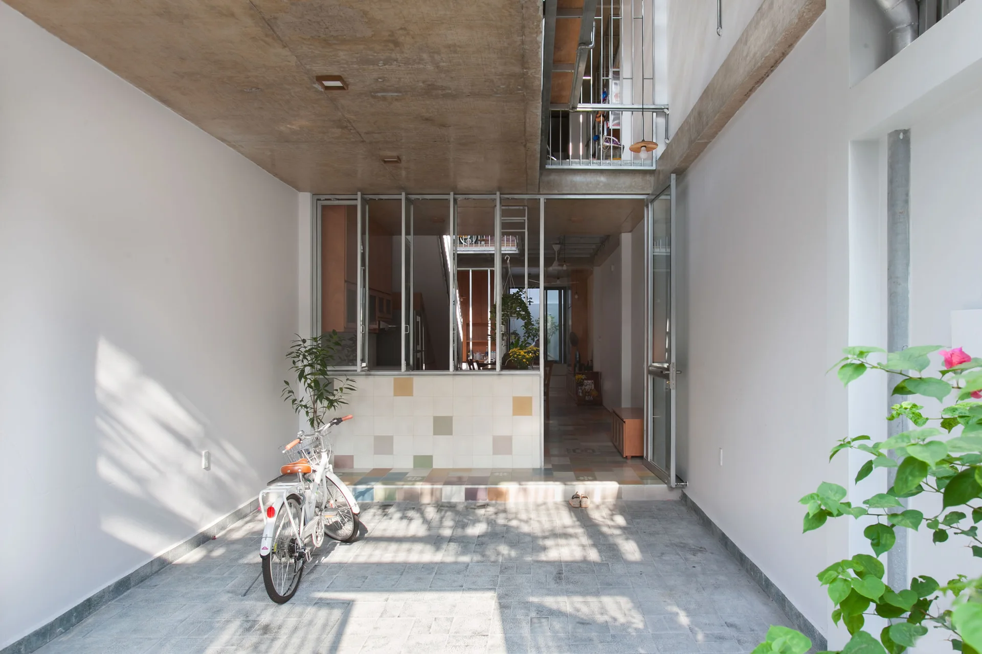 A modern residential entryway with a raw concrete ceiling, gray tiled floors, a parked white bicycle, and a glass partition wall.