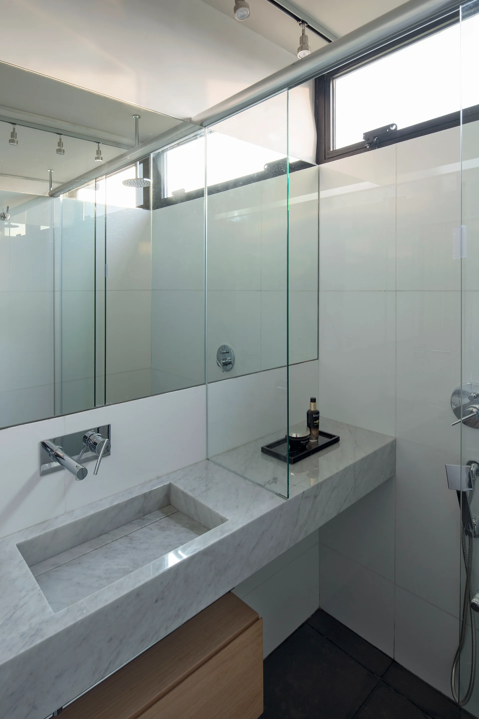 A contemporary bathroom featuring a floating marble vanity with an integrated sink, a wall-mounted faucet, and a clear glass shower partition.