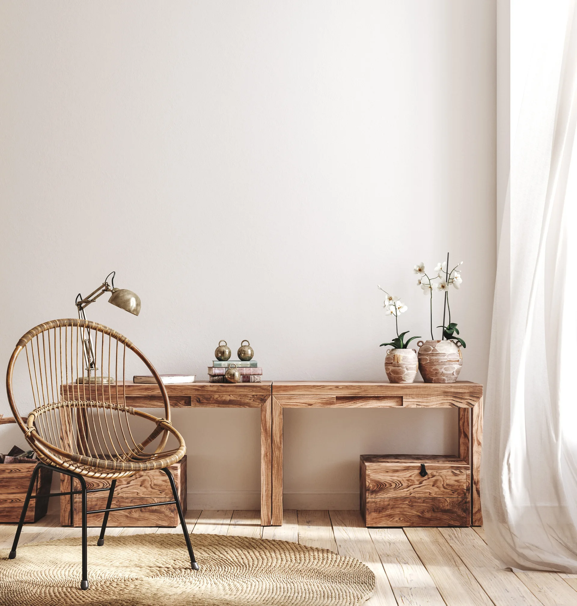A light wood console desk stands against a white wall beside a round woven rug, a rattan chair, and two potted orchids in a sunlit room.