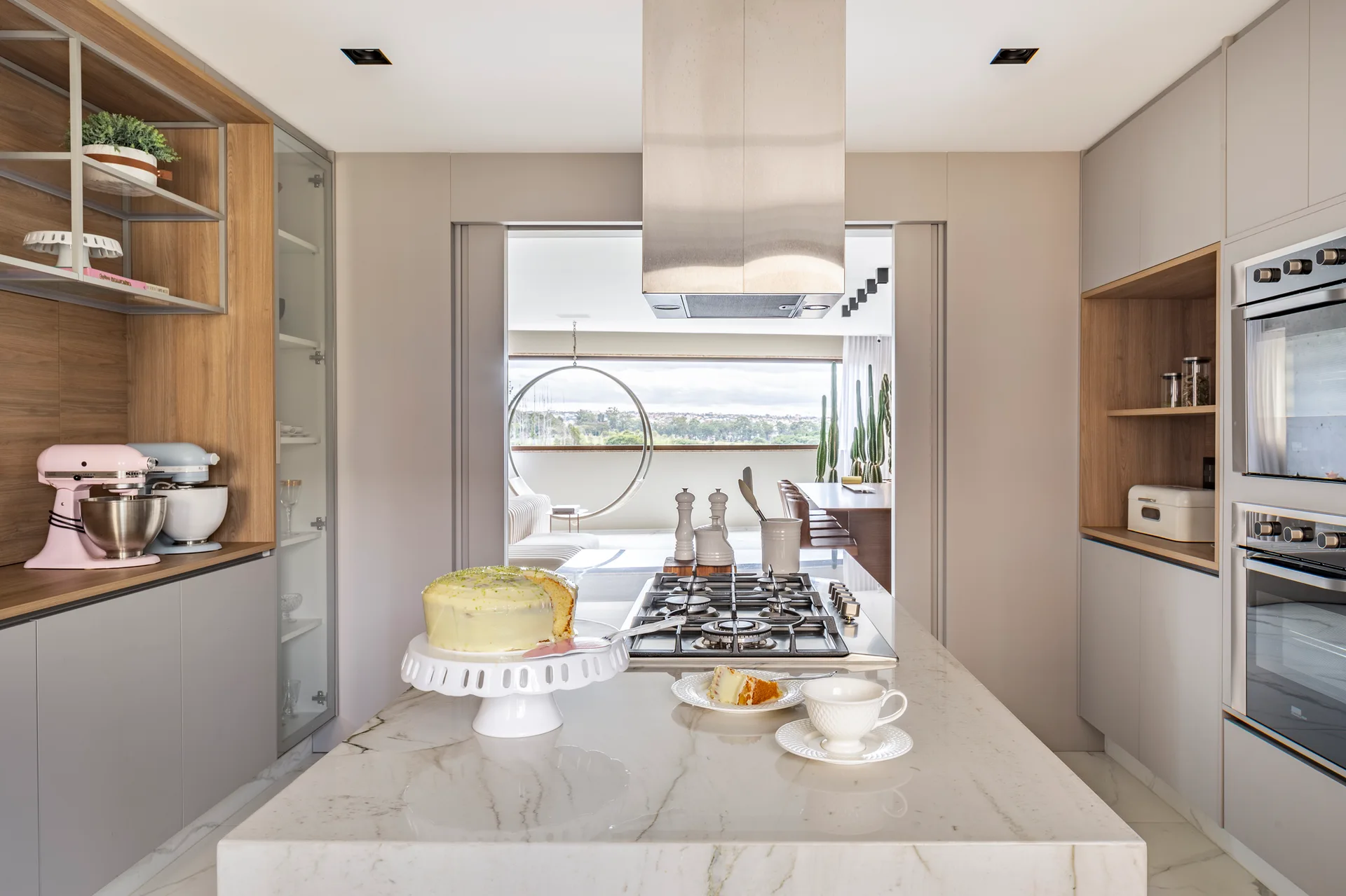 A modern grey kitchen features a marble-topped island with a cooktop, flanked by matte cabinets with built-in wooden shelves.