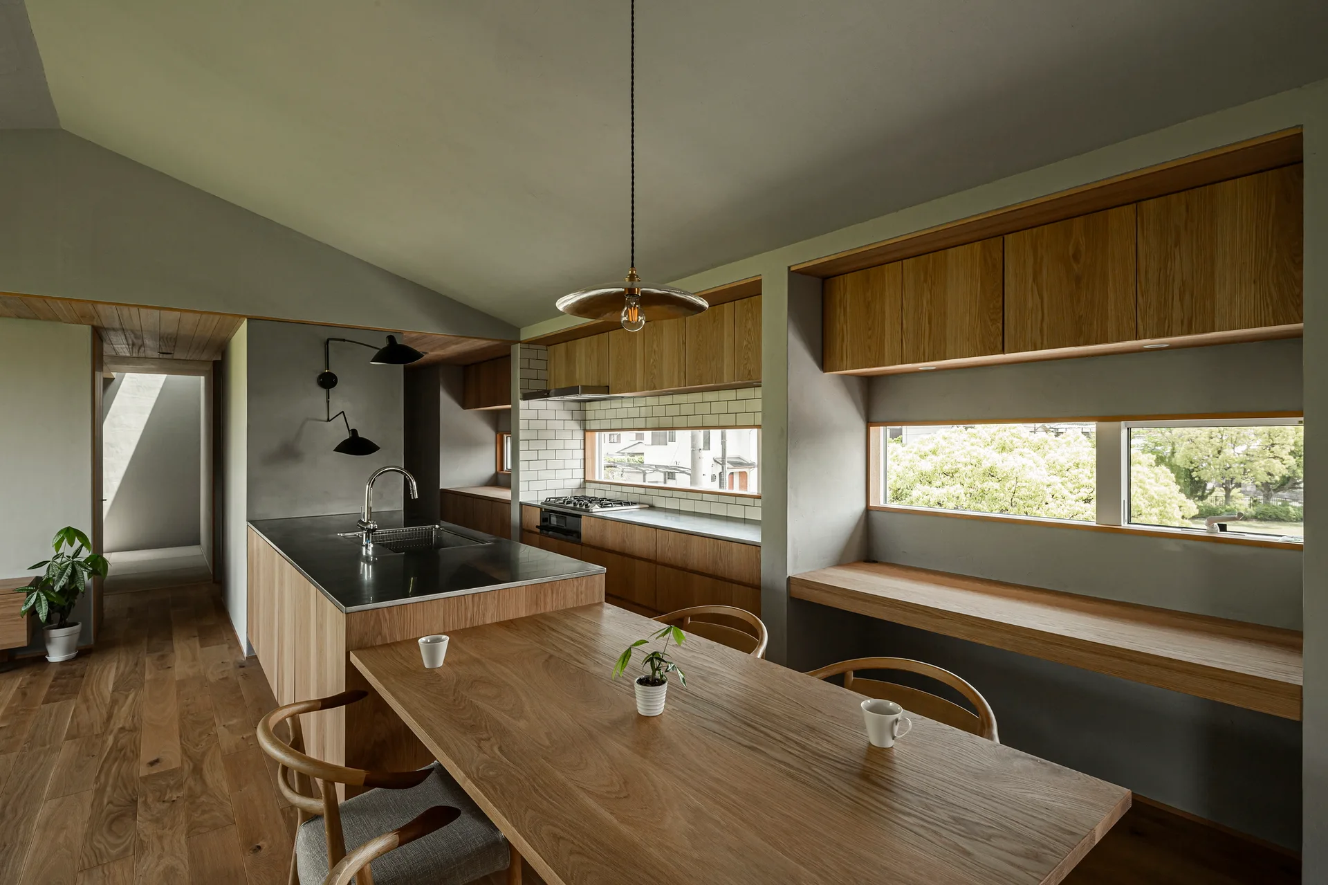 A minimalist kitchen features a wood island with a stainless steel top, an integrated dining table, grey walls, and long horizontal windows.