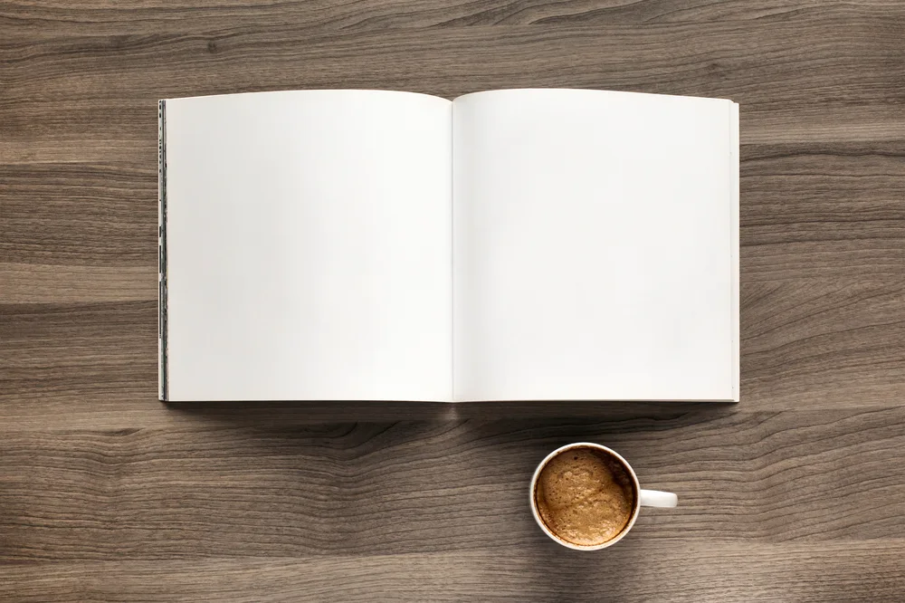 A top-down view of an open blank white notebook and a ceramic cup of coffee on a dark wood grain table.