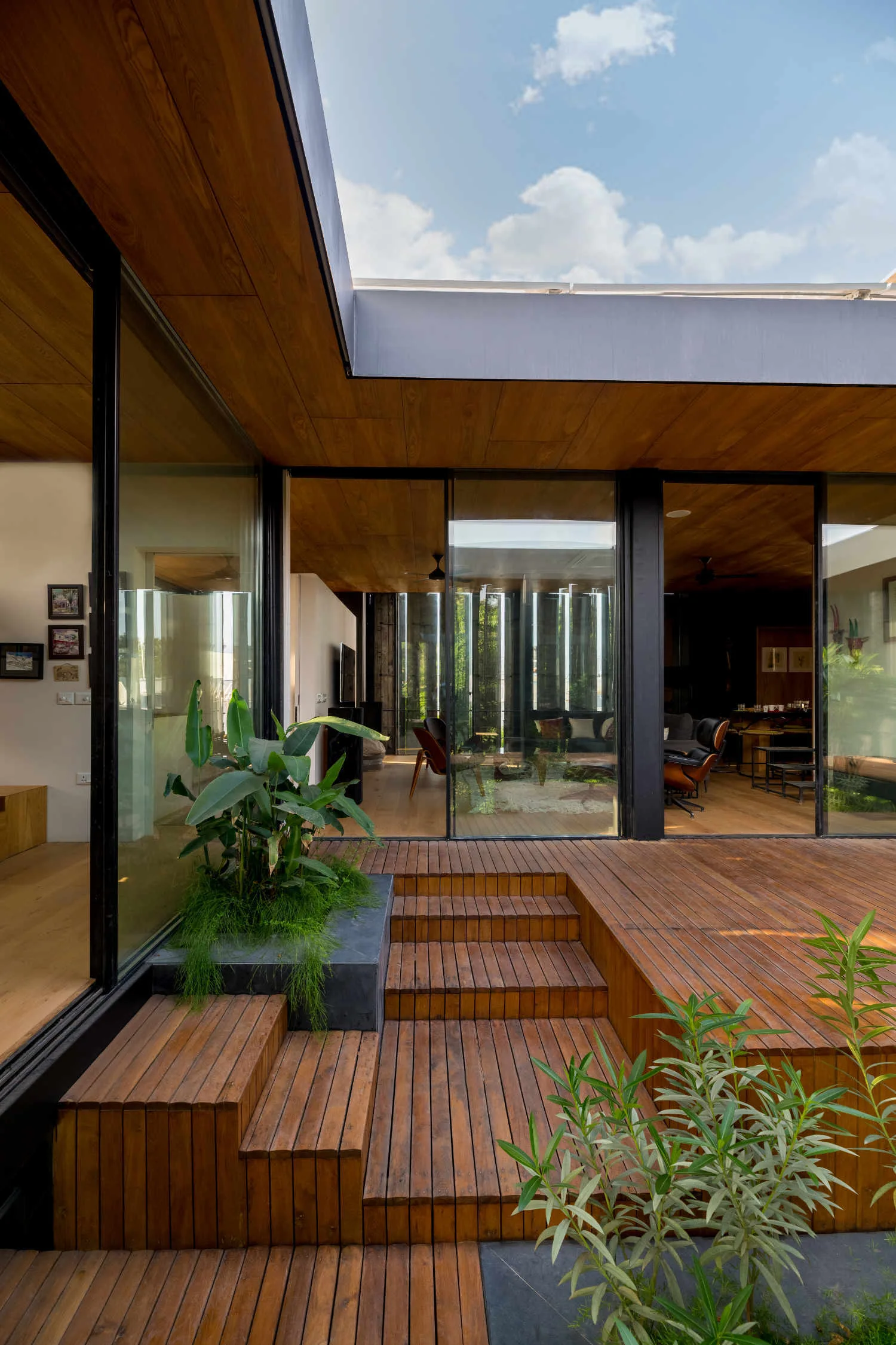 A modern wood-plank patio deck features a set of wide wooden steps leading up to large sliding glass doors and a matching wood-paneled ceiling overhang.