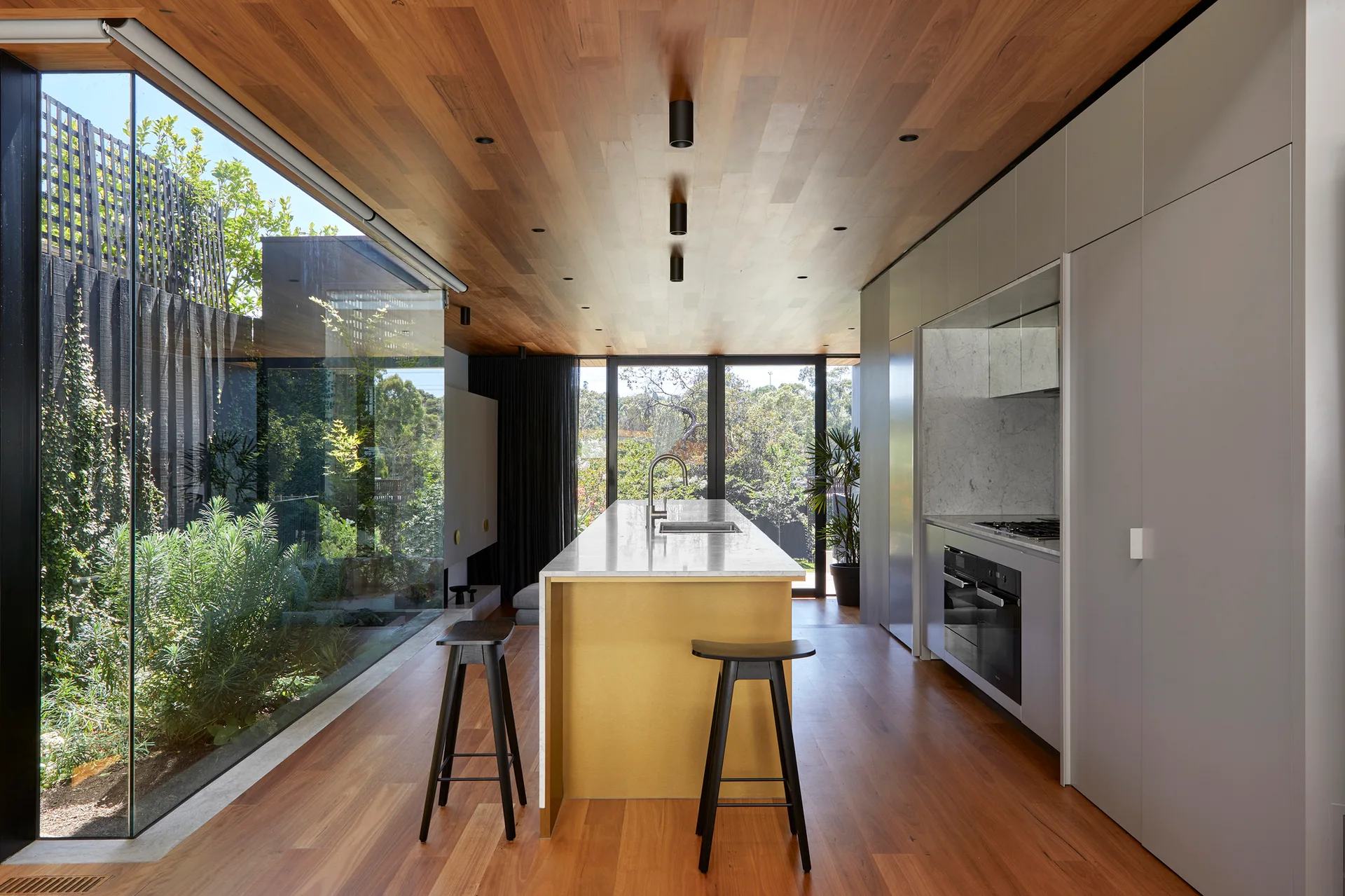 A modern kitchen featuring a central gold-faced island with a marble countertop, black bar stools, and a wood-paneled ceiling.