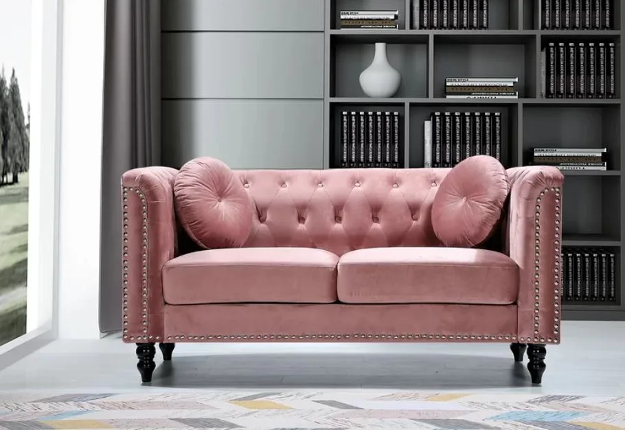 A pink tufted velvet sofa with round cushions stands before a dark grey built-in bookshelf.