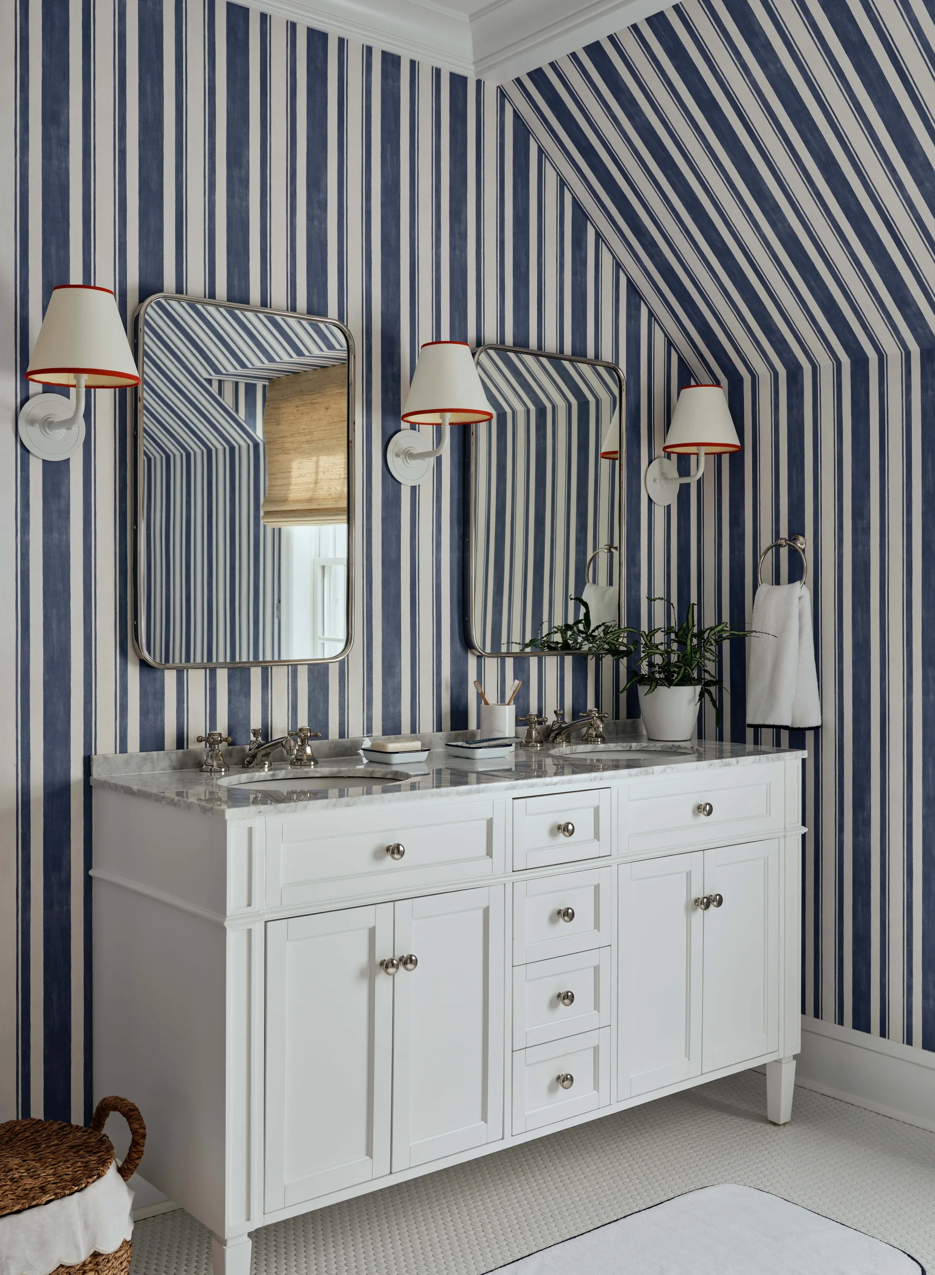 A bathroom double vanity with a marble countertop stands against blue and white striped wallpaper that extends up onto a sloped ceiling.