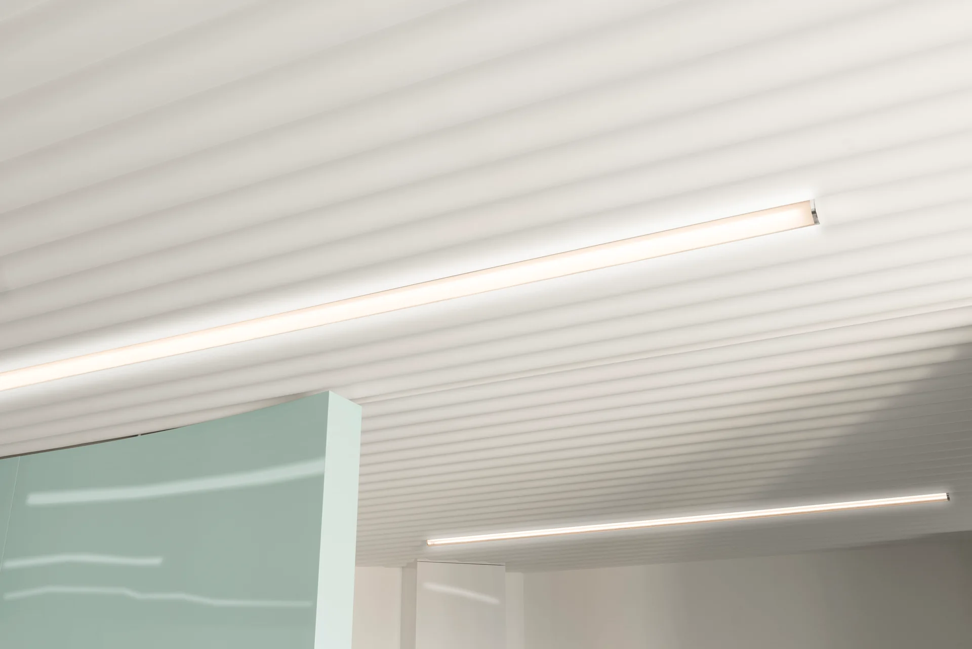 A close-up view of a ribbed white ceiling featuring integrated linear light strips and a smooth mint green partition wall below.