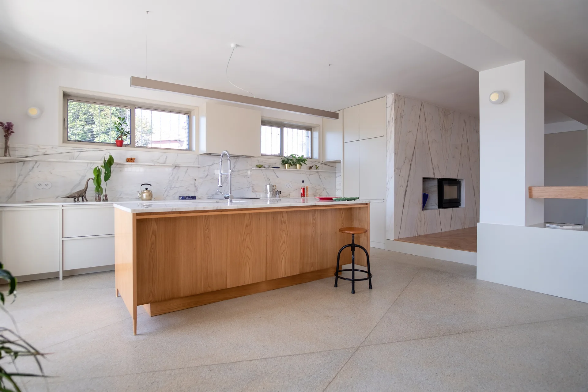 A kitchen featuring a light wood island with marble countertops, white cabinetry, and a nearby marble-clad fireplace wall.