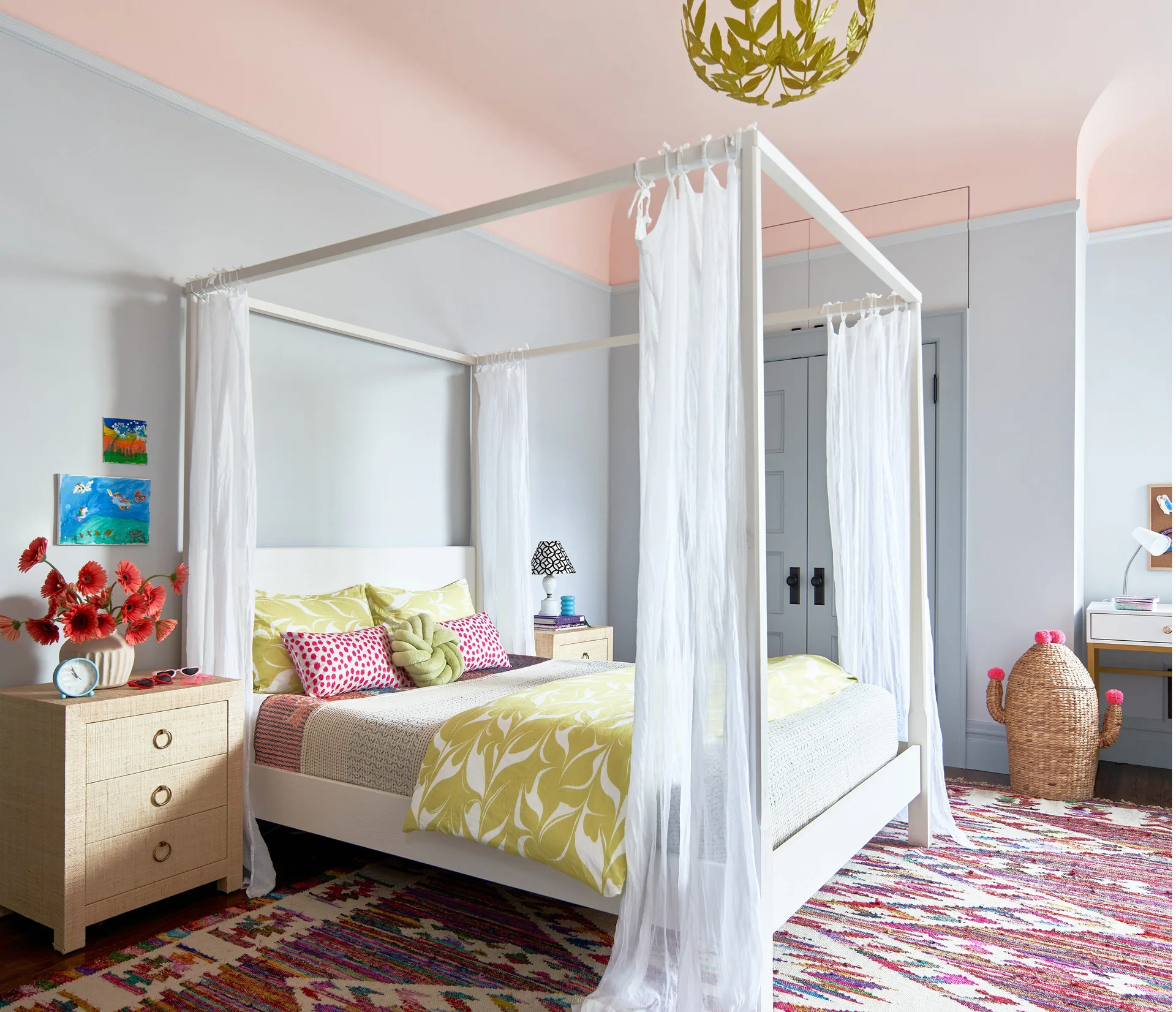 A bedroom features a white four-poster canopy bed with sheer curtains set against light grey walls and a pale pink ceiling.