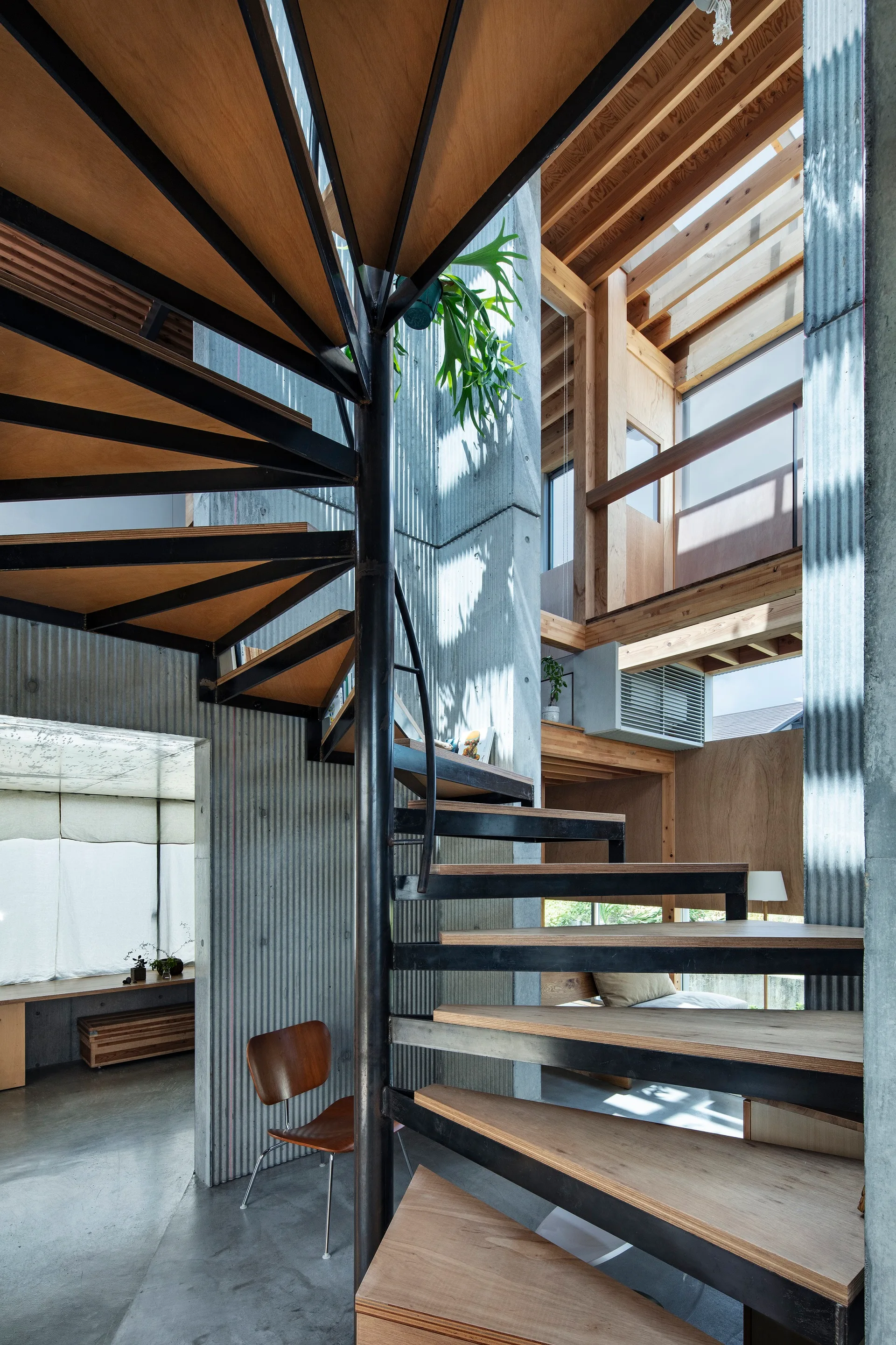 A modern industrial home interior features a central black metal and wood spiral staircase against corrugated grey concrete walls.