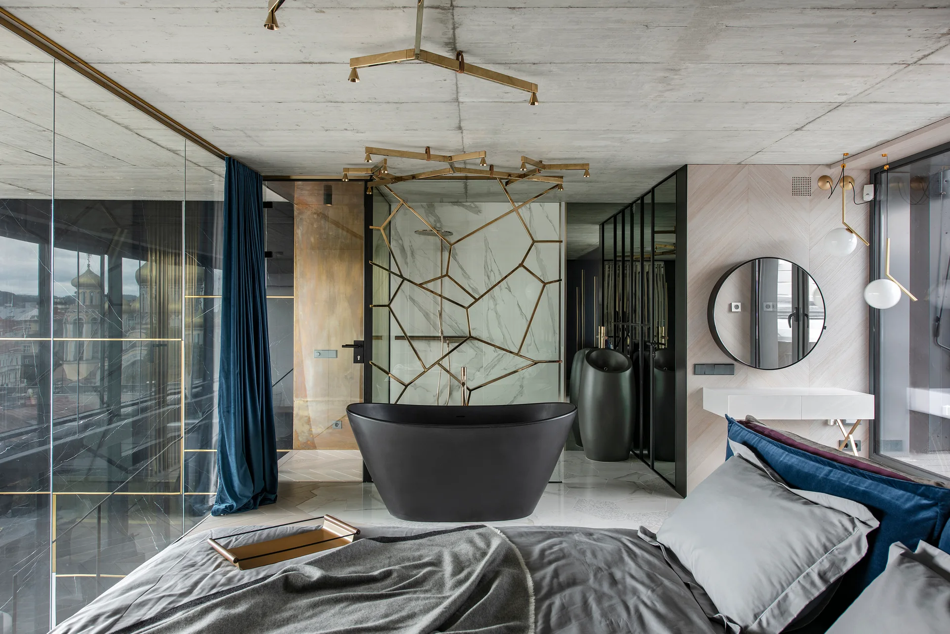 A modern bedroom suite featuring a grey bed in the foreground and an open-concept bathroom with a matte black freestanding tub and a geometric marble partition.