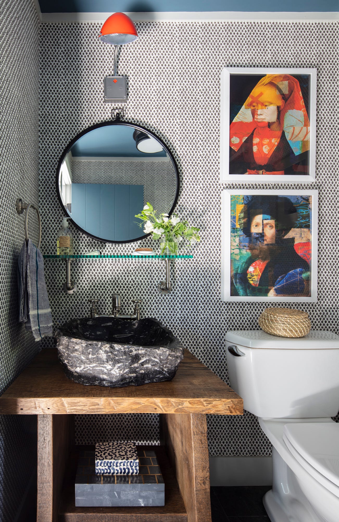 A powder room features a rough-carved stone basin sink on a rustic wood vanity against black and white patterned wallpaper.