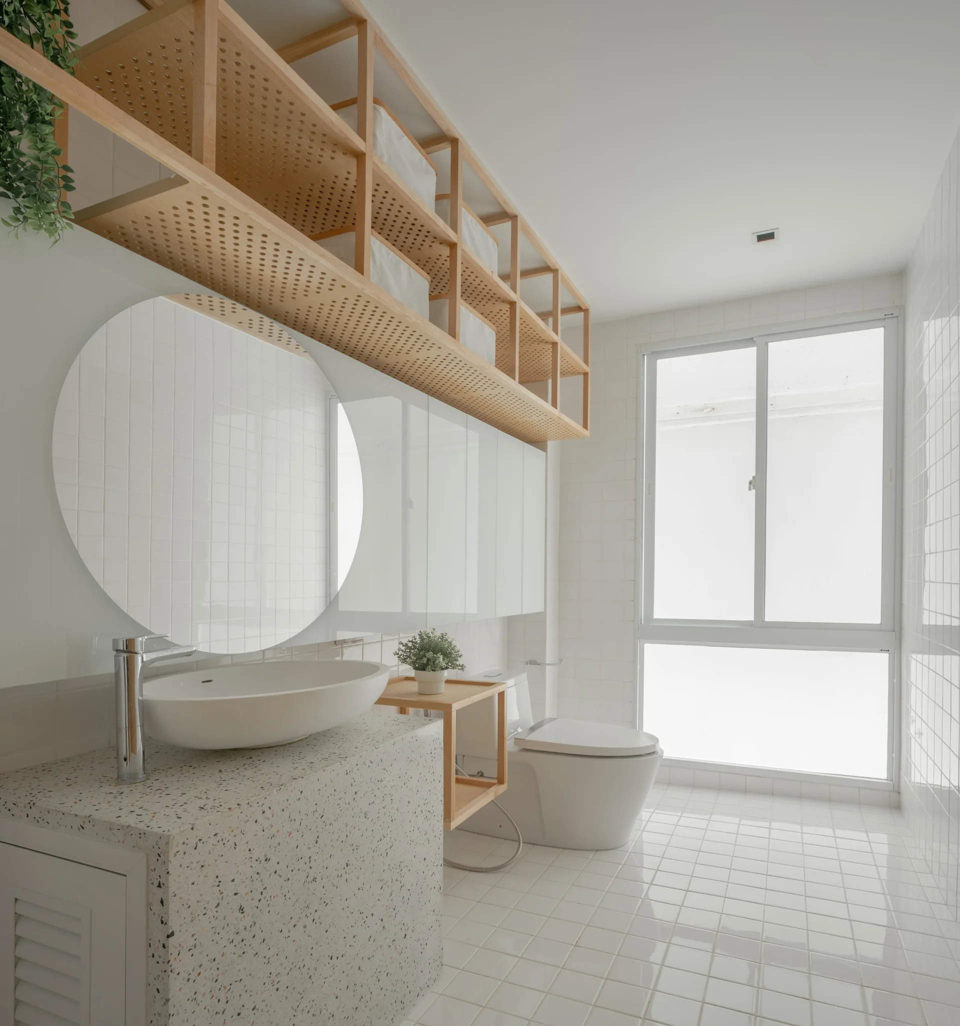 A modern white tiled bathroom featuring a speckled terrazzo vanity with a vessel sink, a round mirror, and open wooden shelving.