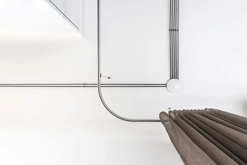A close-up view of a white ceiling showing black electrical conduits and a curved metal curtain track with pleated brown drapes.