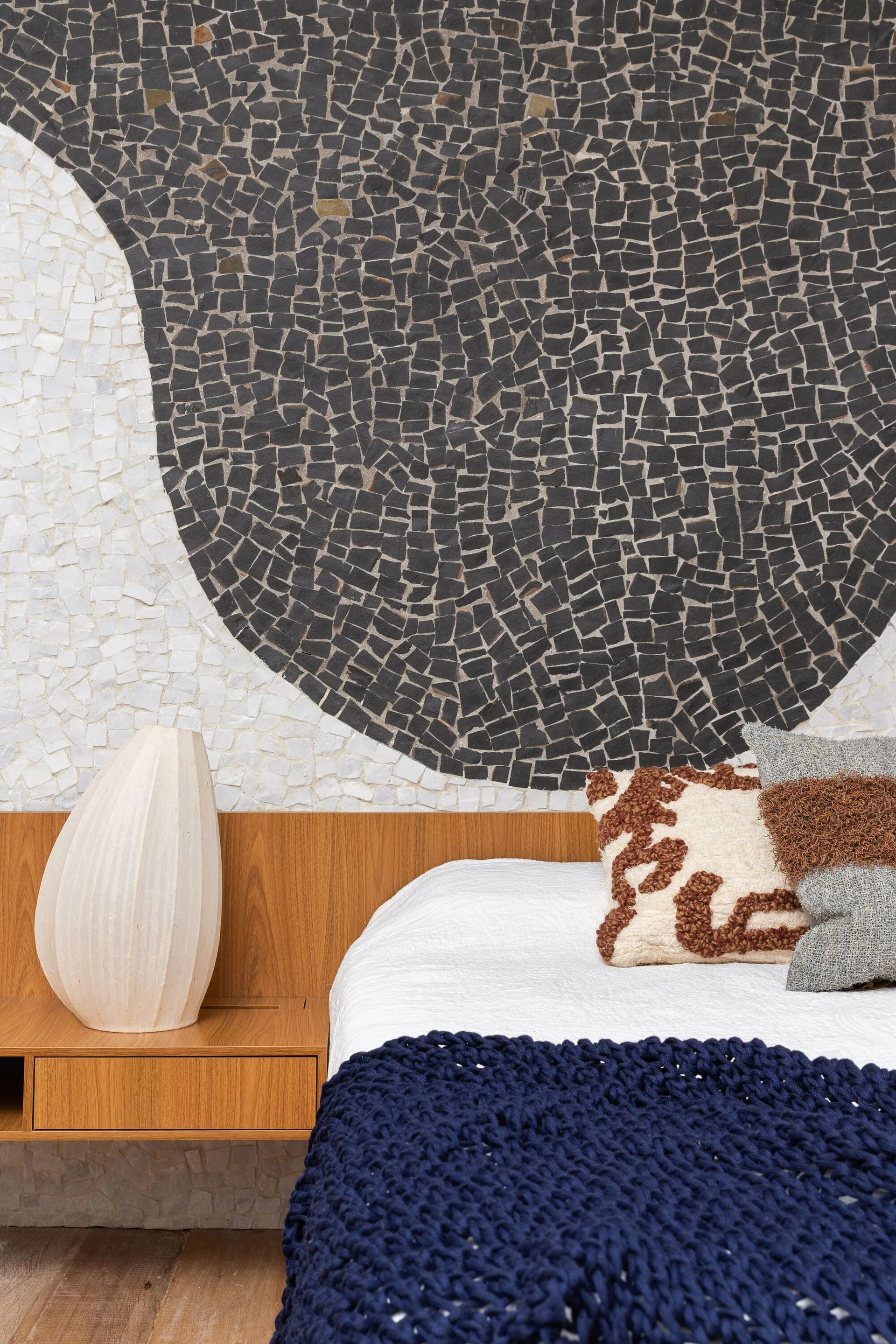 A bedroom corner features an integrated wooden headboard and floating nightstand set against an abstract black and white tile mosaic accent wall.