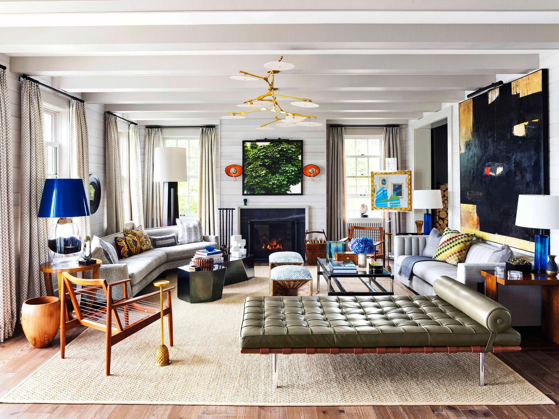 Spacious living room featuring white planked walls, a fireplace, grey sofas, a green leather daybed, and a brass chandelier.